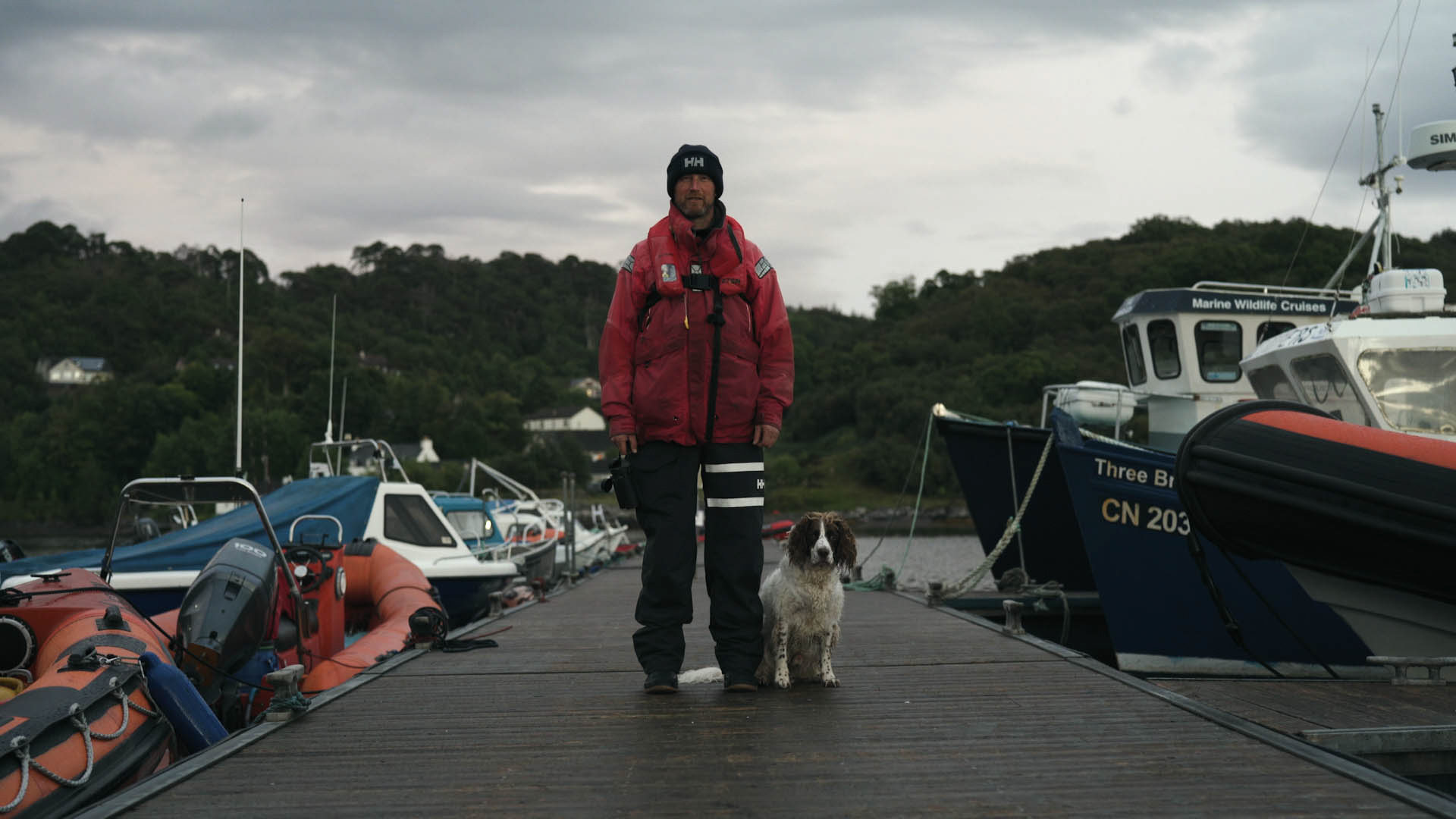 Steve Truluck wearing a red waterproof coat standing on a quay with his dog, a still taken from the short film Truluck by Matt Cannon and Jake Smallwood