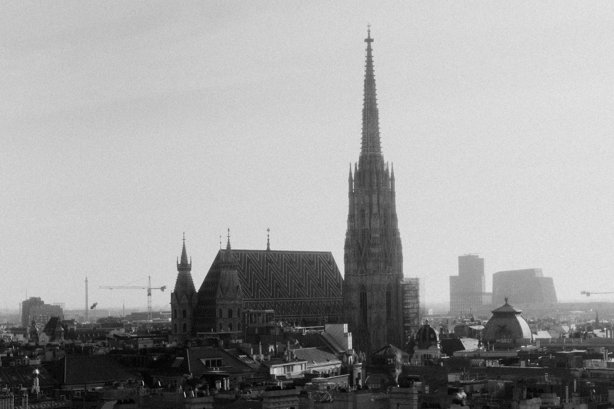 Black-and-white photograph of St Stephen’s Cathedral in Vienna, with its striking south tower rising above the rooftops of the city centre. Shot by Dhan Limwattana.