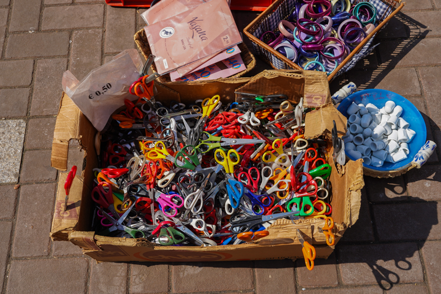 Een kleurrijke doos met verschillende scharen op de Amsterdamse Waterloopleinmarkt, vastgelegd in helder zonlicht met typische marktdetails, gefotografeerd door Louise Kluit