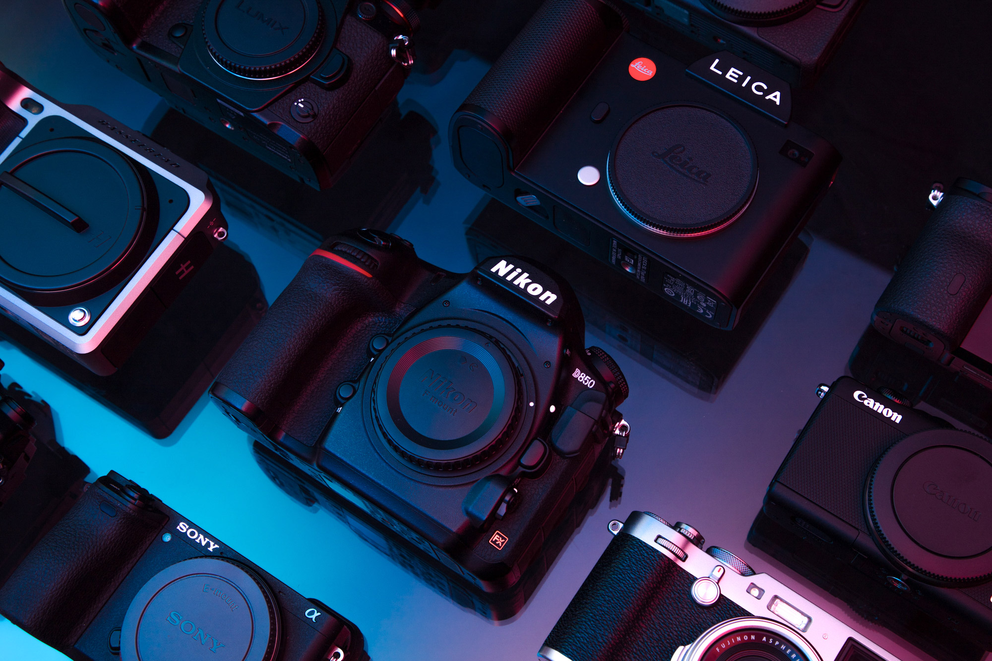 Flatlay of various digital cameras against a glass background lit from the sides by blue and red lights

