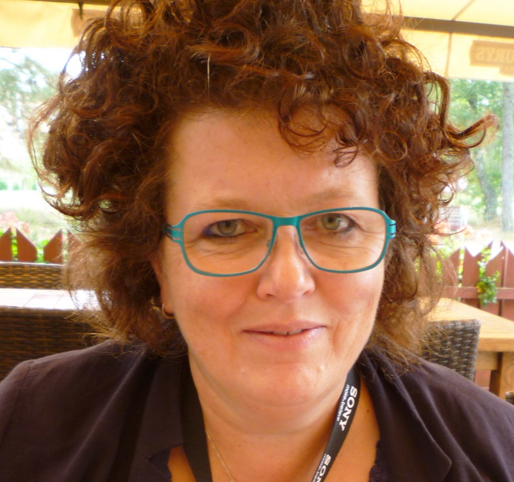 A portait photo of Anna Fox wearing blue glasses and a dark top