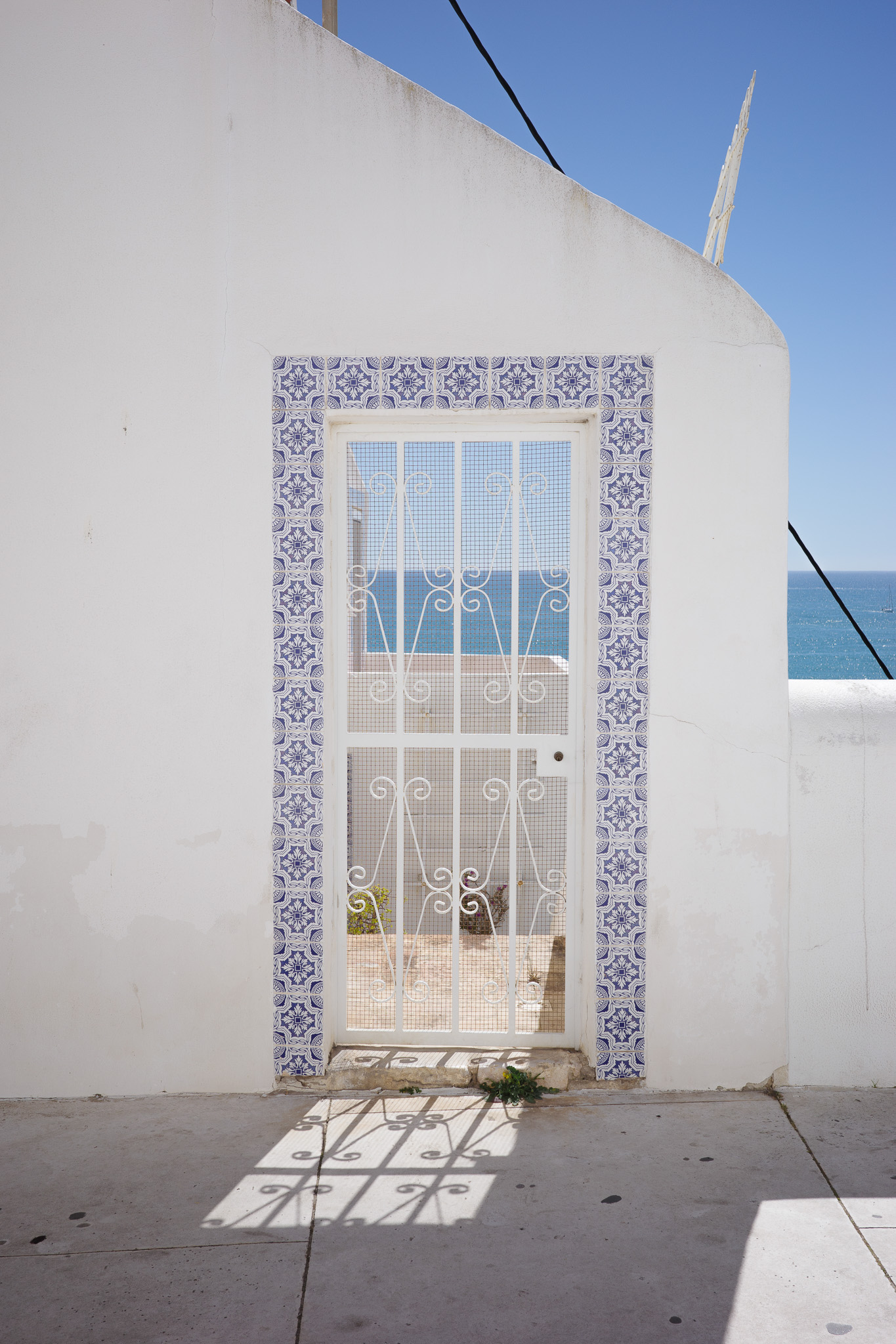 Een metalen poort die leidt naar een balkon dat uitkijkt op de zee in Albufeira, Portugal, gefotografeerd door Connor Redmond.
