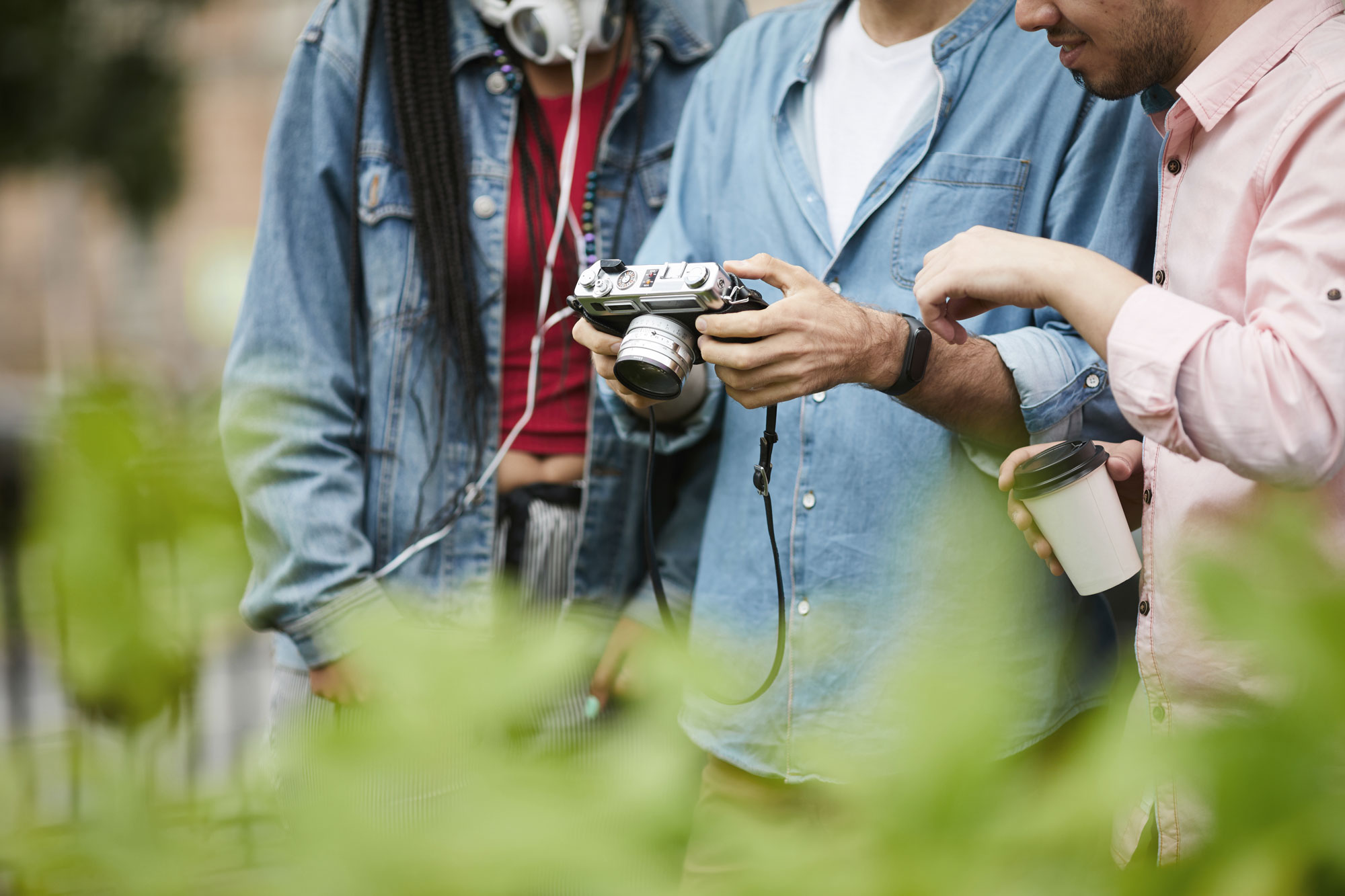Three people looking at the photos on a camera, with leaves from a tree in the foreground.