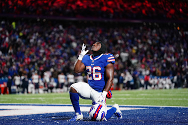Jugador de fútbol arrodillado y mirando hacia el cielo, vistiendo el número 26 en una camiseta azul.