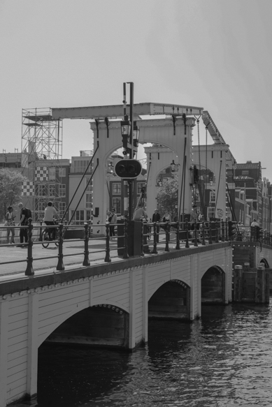 Een zwart-witbeeld van de Amsterdamse Magere Brug, met fietsers en voetgangers die de iconische brug over de Amstel oversteken, gefotografeerd door Louise Kluit