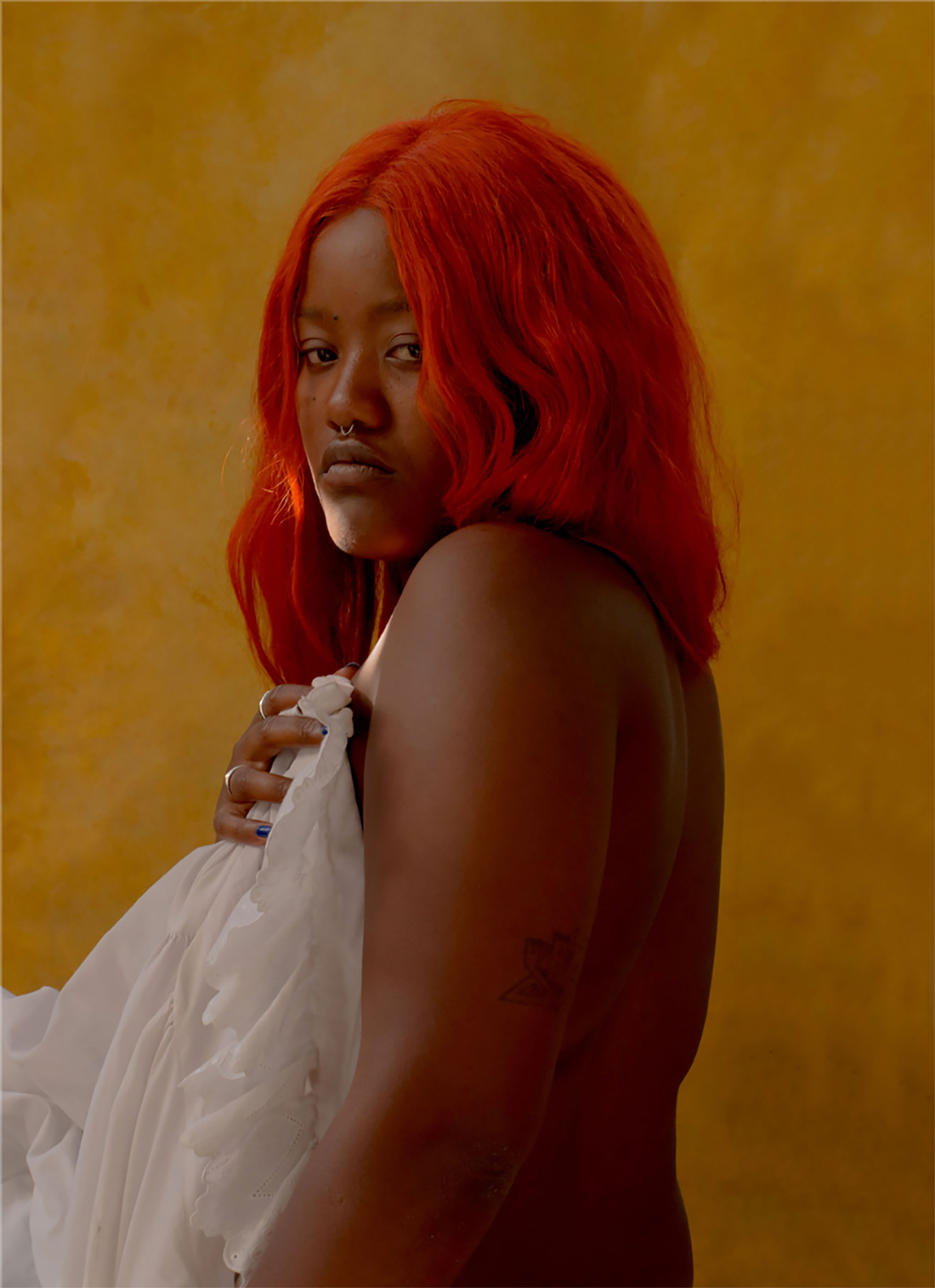 Black woman with red dyed hair covering her naked upper body with a white piece of cloth, shot by Nicole Benewaah