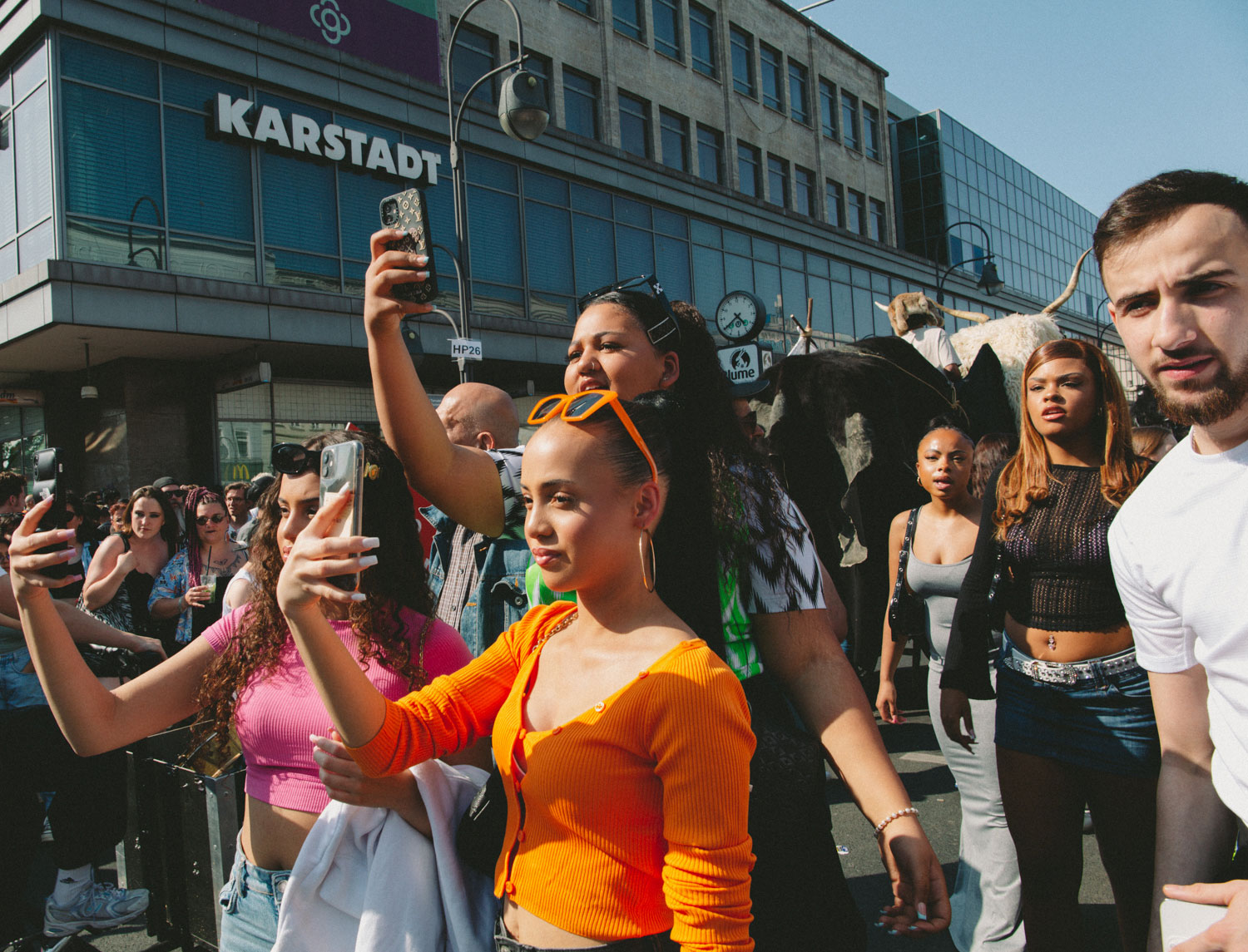 Three people in the centre of the picture filming with their smartphones, next to them other people, KARSTADT building in the background, shot by Stefanie Schmid Rincon with the Canon EOS R6.