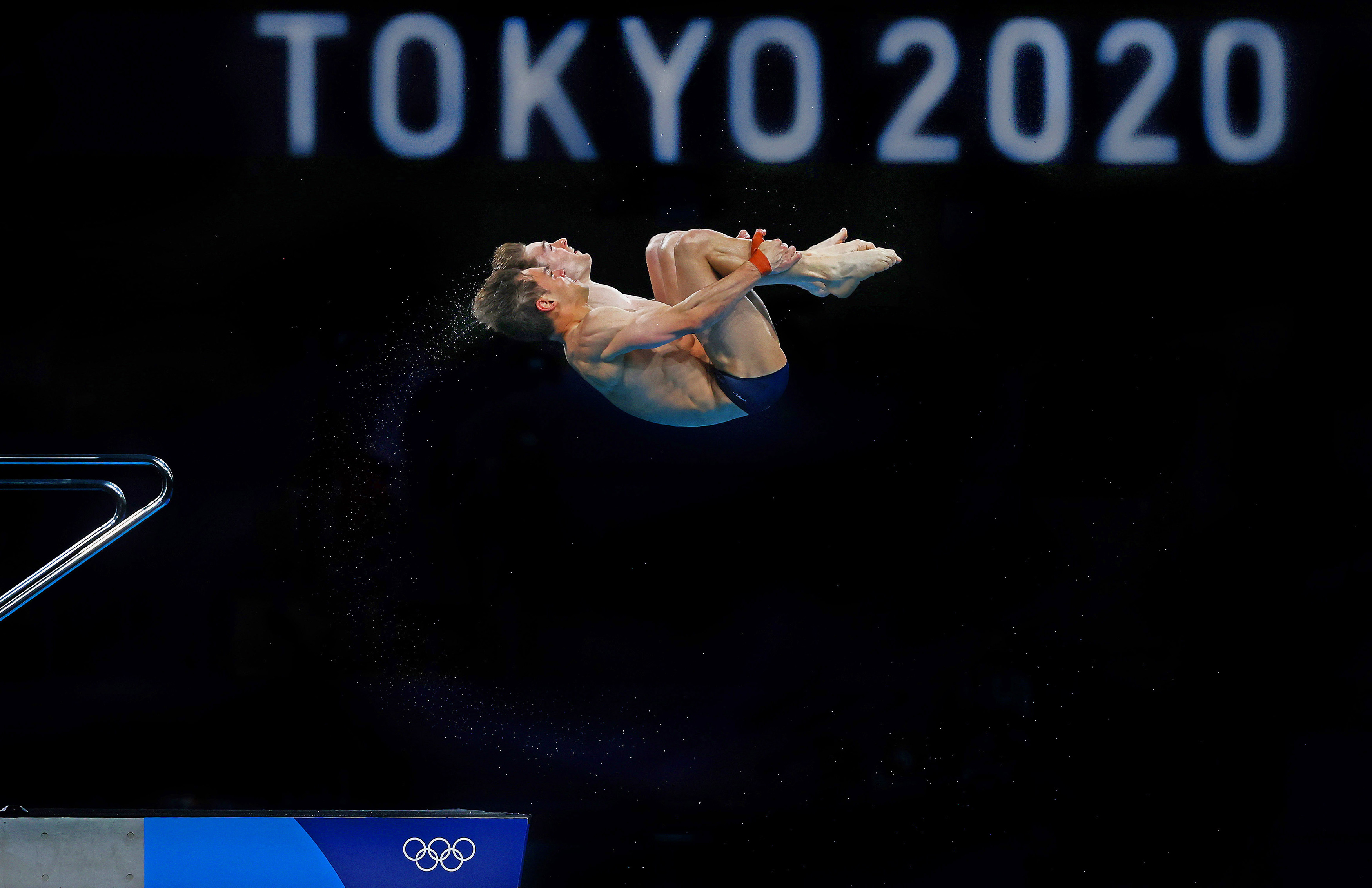 Image of an Olympic diver doing a backflip with the Tokyo 2020 Olympic sign in the background.