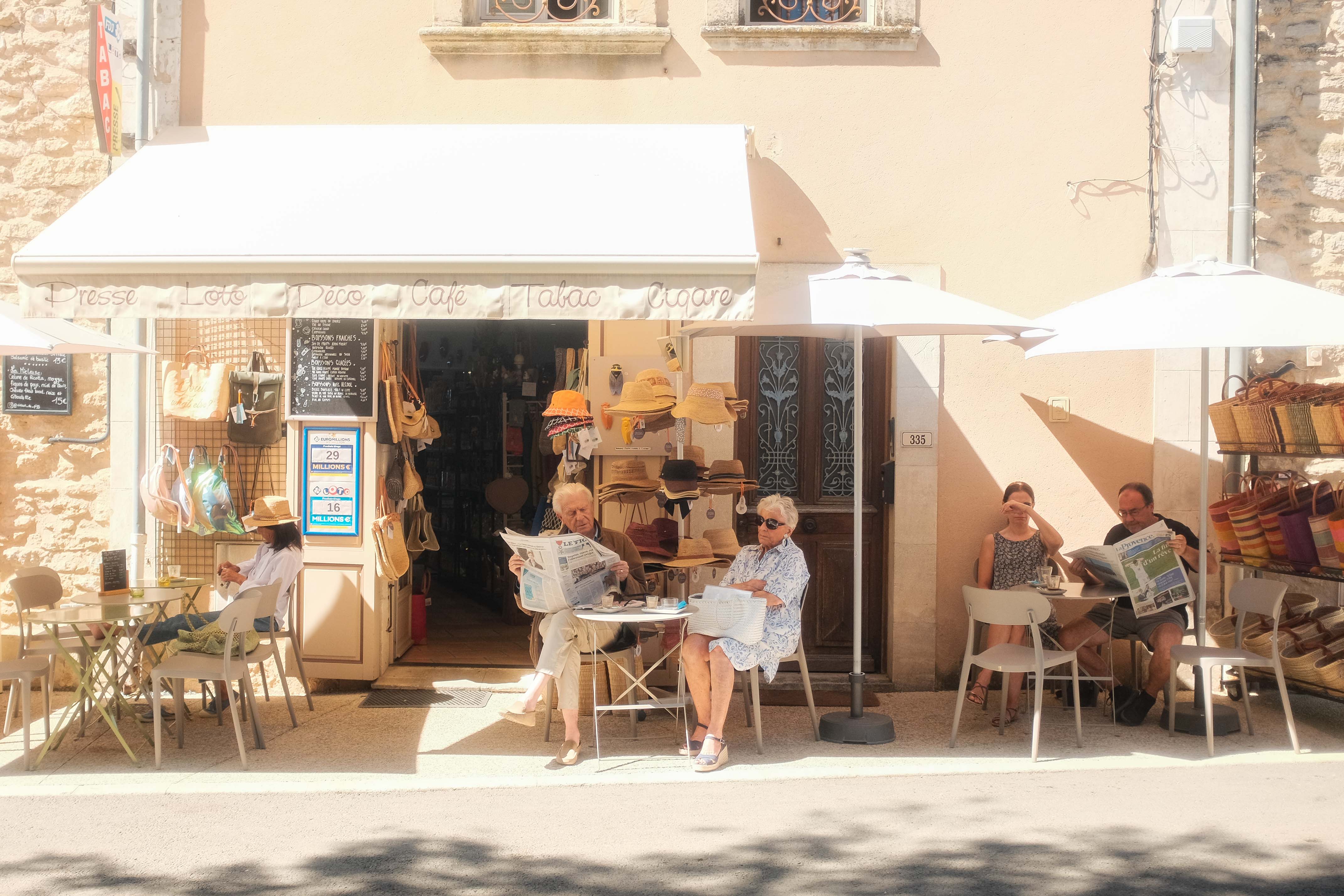 A bright scene of a cafe in Gordes, France, with an elderly couple reading the newspaper. Taken on the Fujifilm X100T by Connor Redmond.