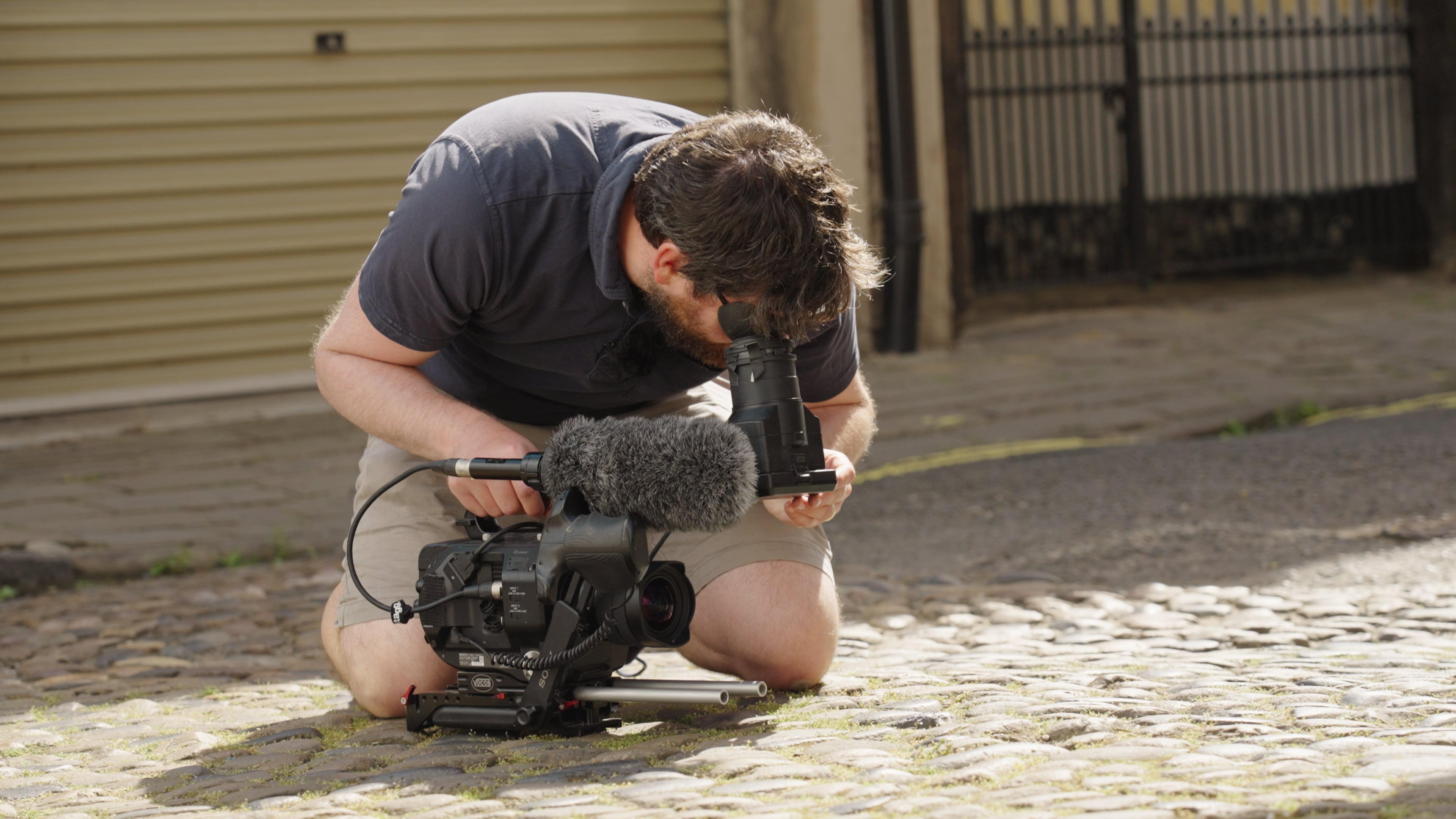 Le producteur-réalisateur de télévision Steve Morgan, agenouillé dans une rue pavée de Yorke, regarde à travers l'oculaire d'un Sony FS7.