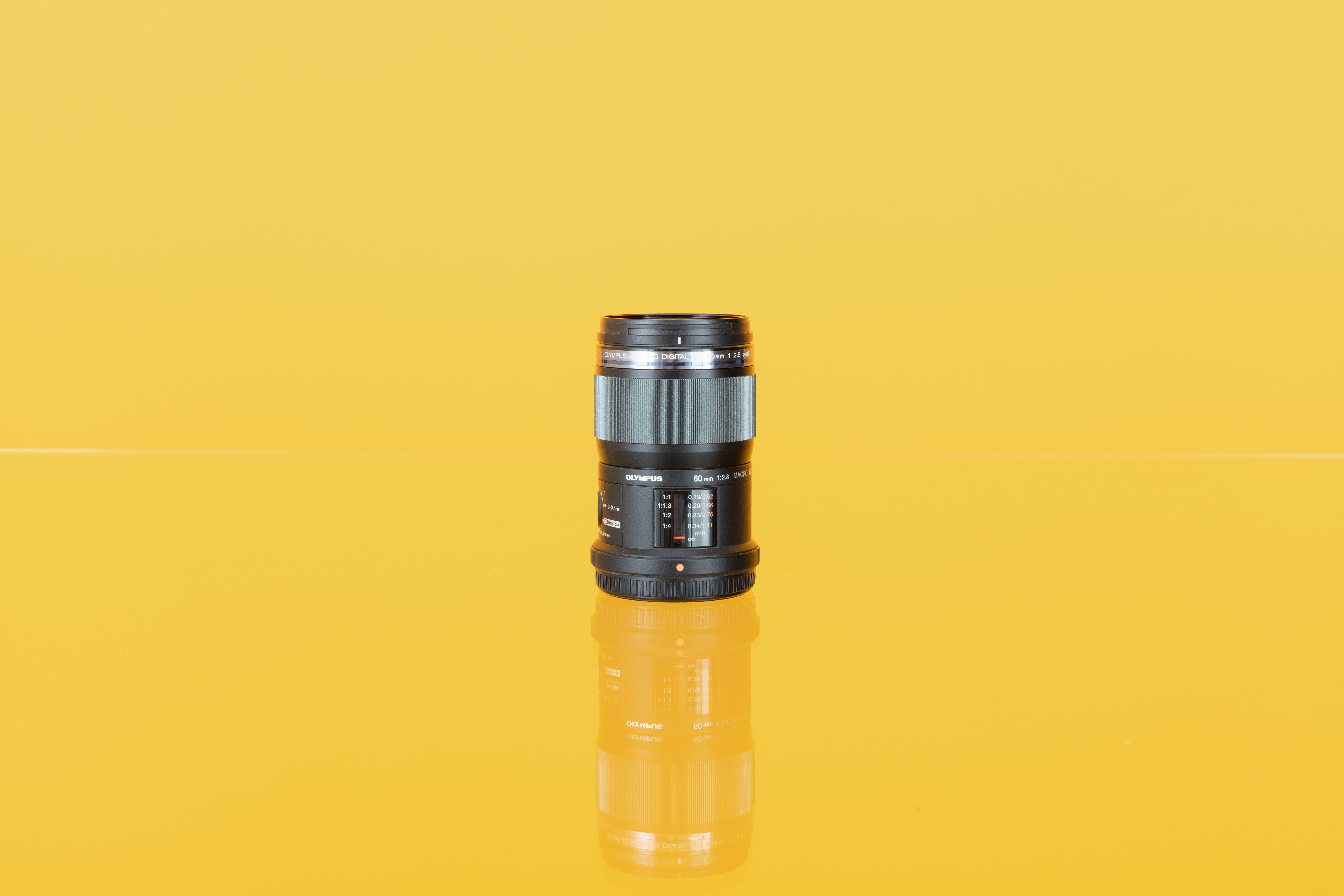 Image of an Olympus M.Zuiko Digital ED 60mm f/2.8 Macro lens on a yellow background.