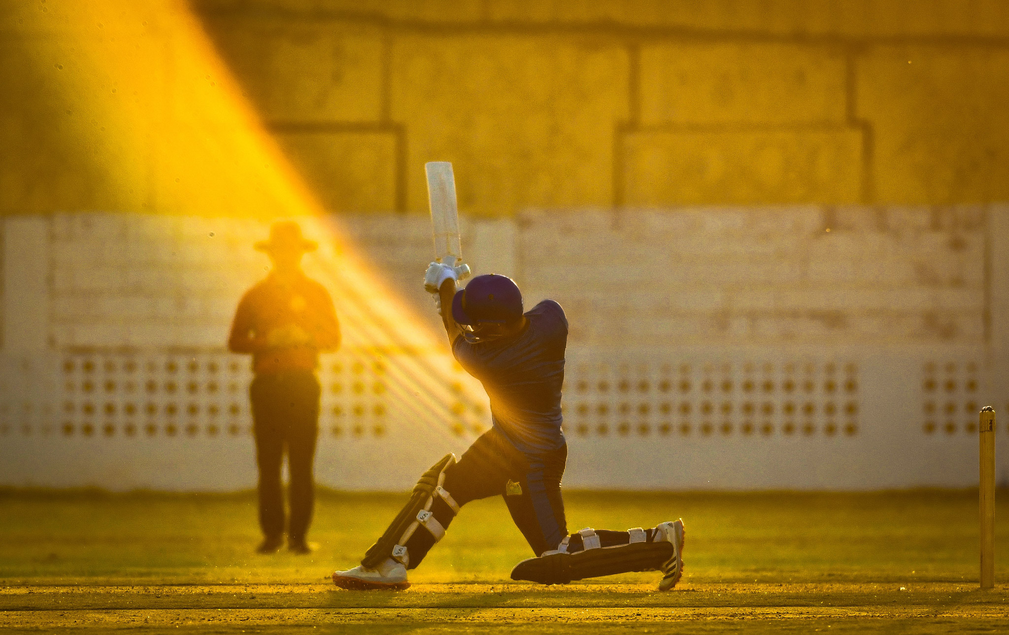 Cricketer wings his bat after hitting a ball and a sun glare makes it looks as if there is a trail where the ball would be