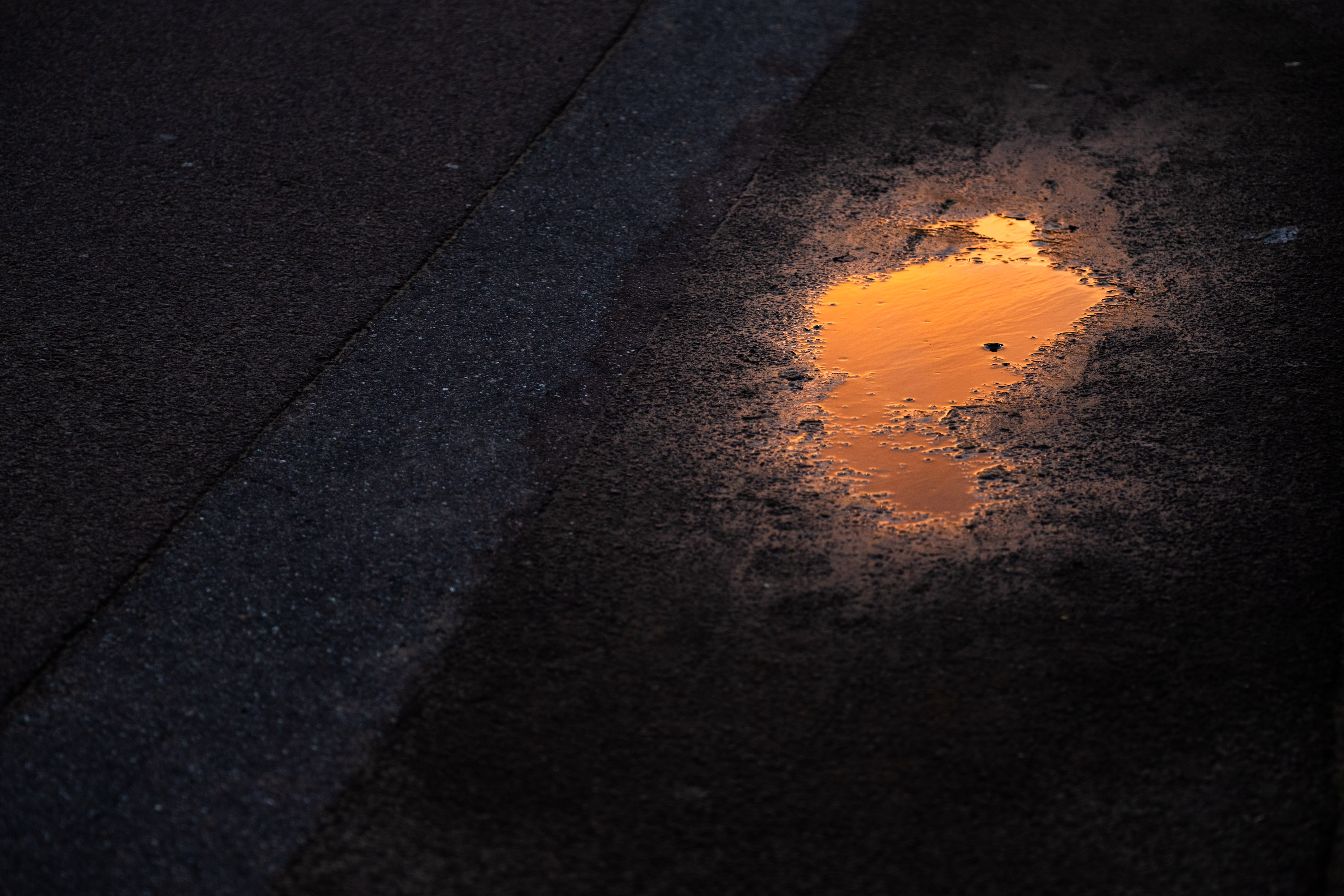 Une flaque d'eau sur un trottoir goudronné reflète un ciel orange. Photo prise par un shot Fujifilm X-T5