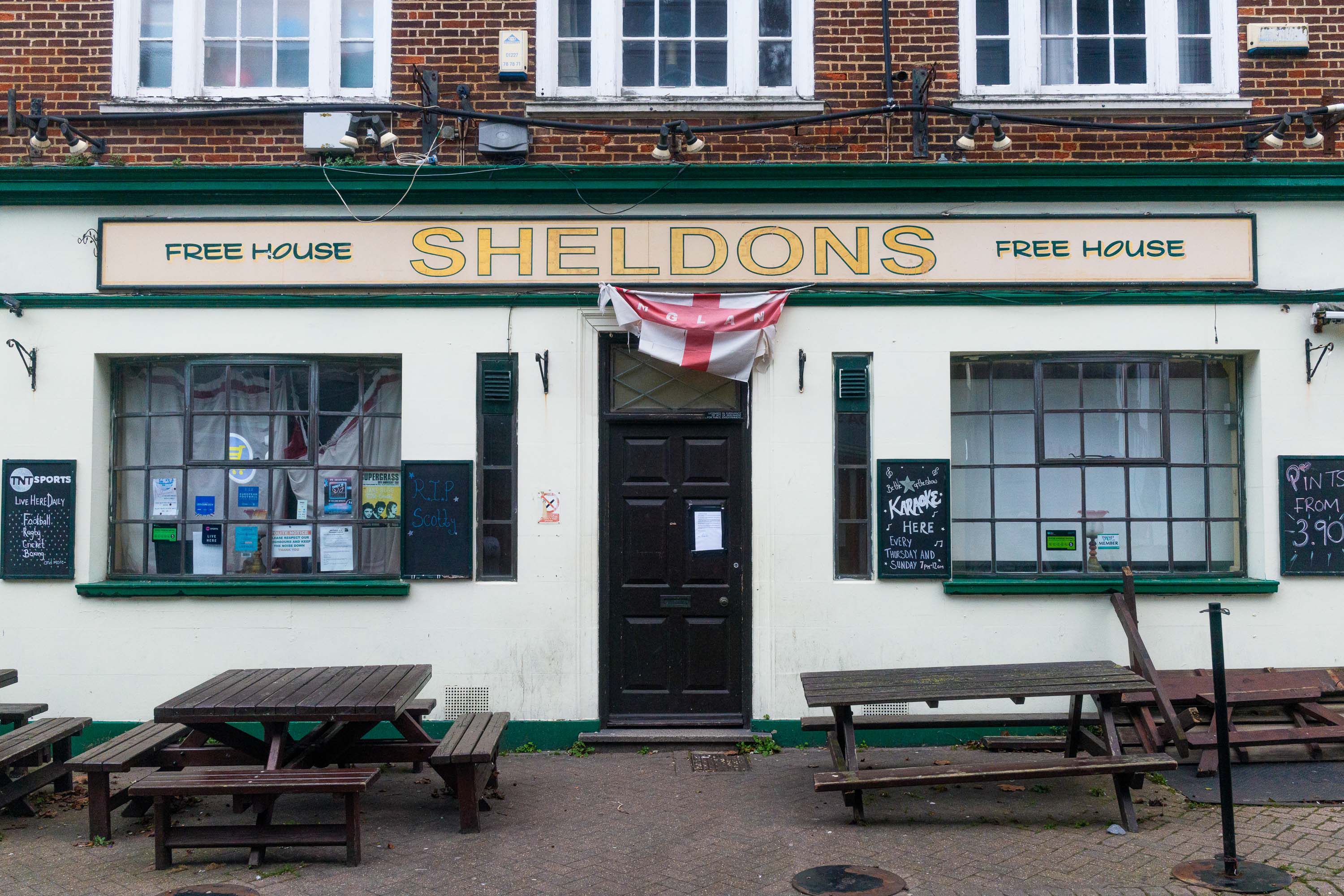 Bei weichem, bedecktem Licht fotografierte Fassade eines traditionellen Pubs namens „Sheldons“ mit der englischen Flagge über dem Eingang. Aufgenommen von Connor Redmond mit einer Sony RX1R III.