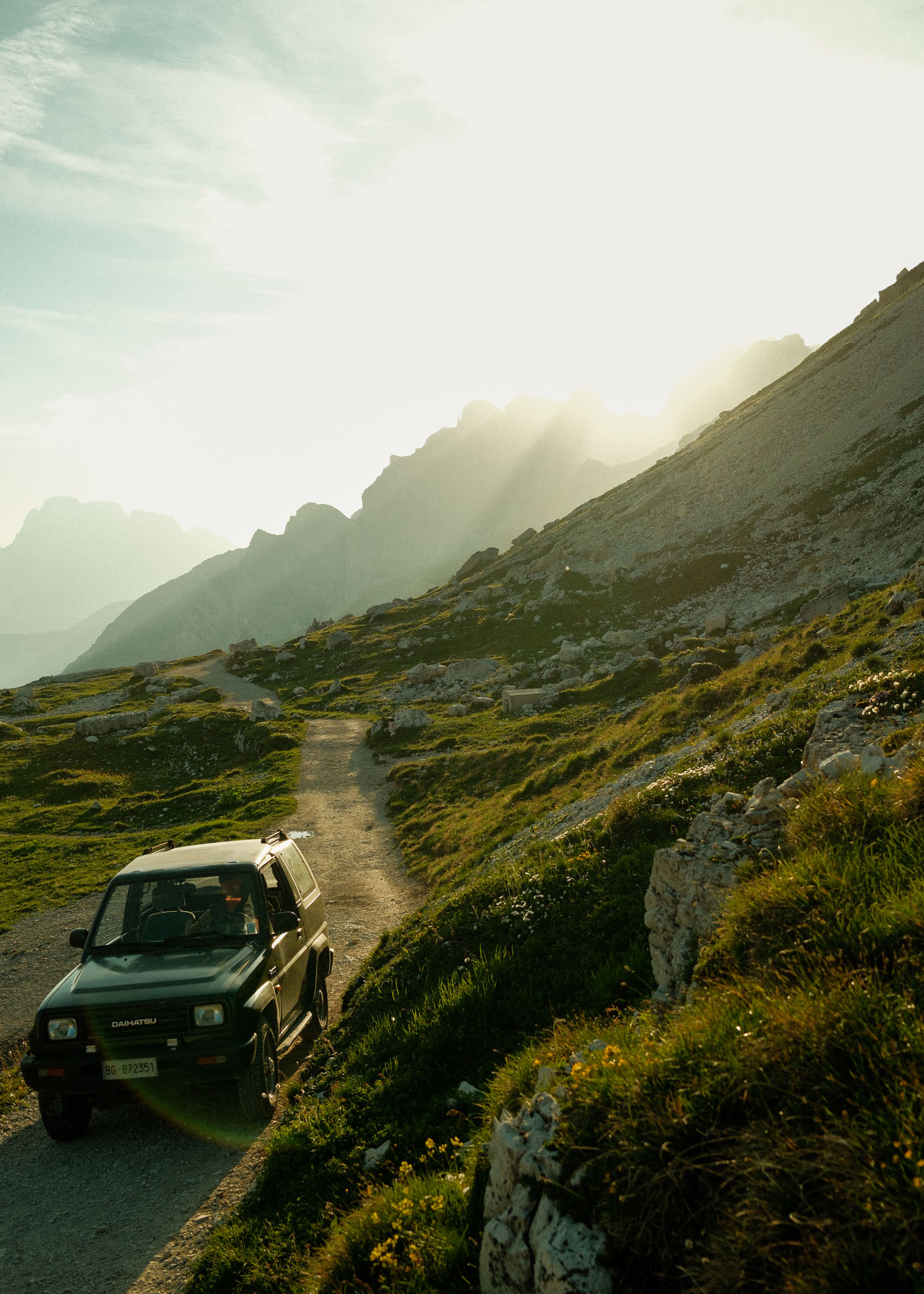 A 4x4 drives through an Alpine environment with the sun bright in the background. Taken on the Fujifilm X100VI by Hermann Furin.