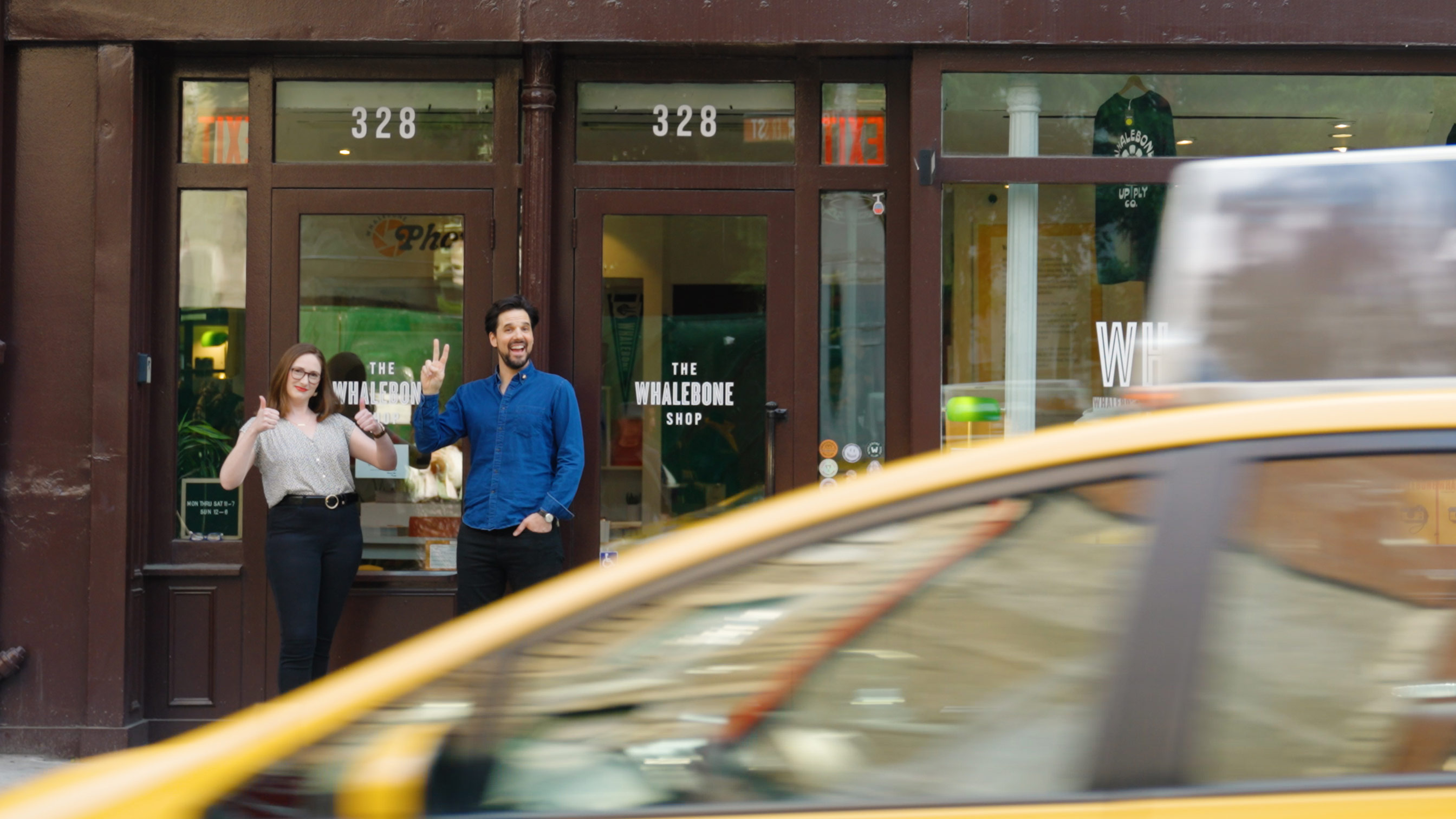 Wally Koval and Marjorie Becker giving a peace sign and two thumbs up, respectively, outside a building.