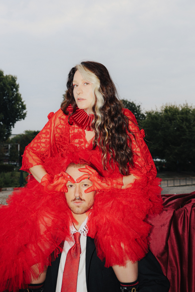 Creative portrait of a couple in vibrant red couture, blending art, fashion, and theatrical flair. Shot by Marina Polovinkina on a Canon EOS R6 Mark II.