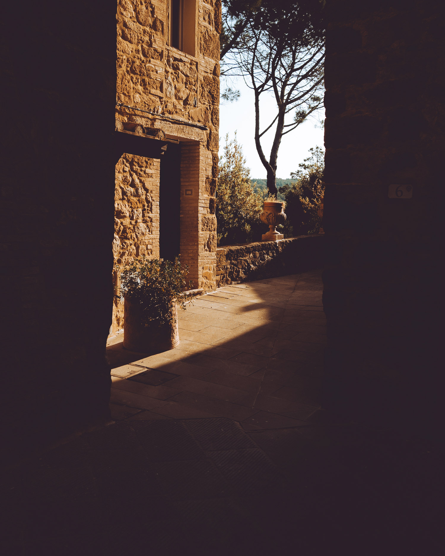 A wall in Petrolo, Tuscany. The foreground is covered in shadow, with a tree and and fields in the background.