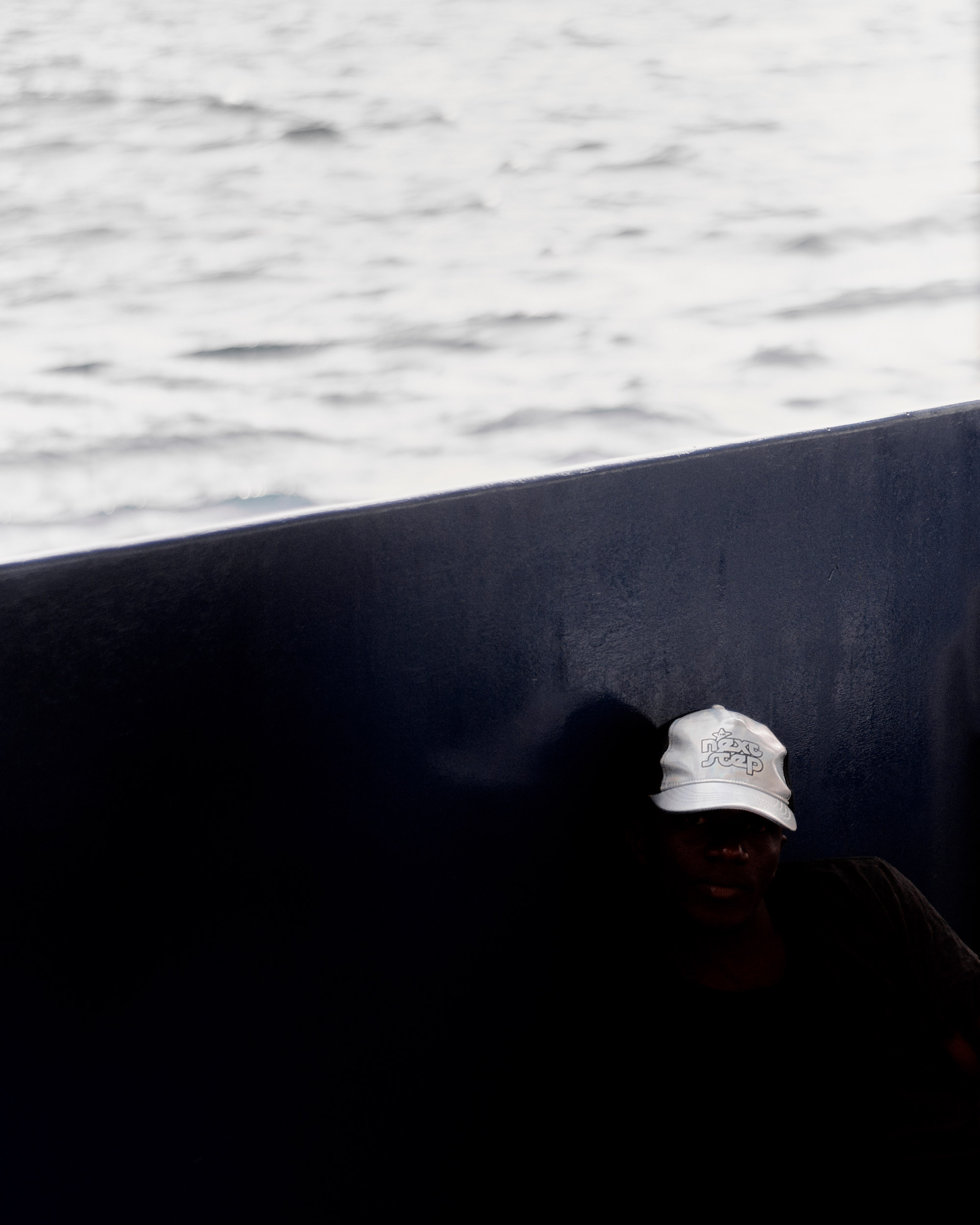 Foto einer Person mit weißem Cap auf dem “next step” steht, die auf dem Boden eines Schiffes sitzt.