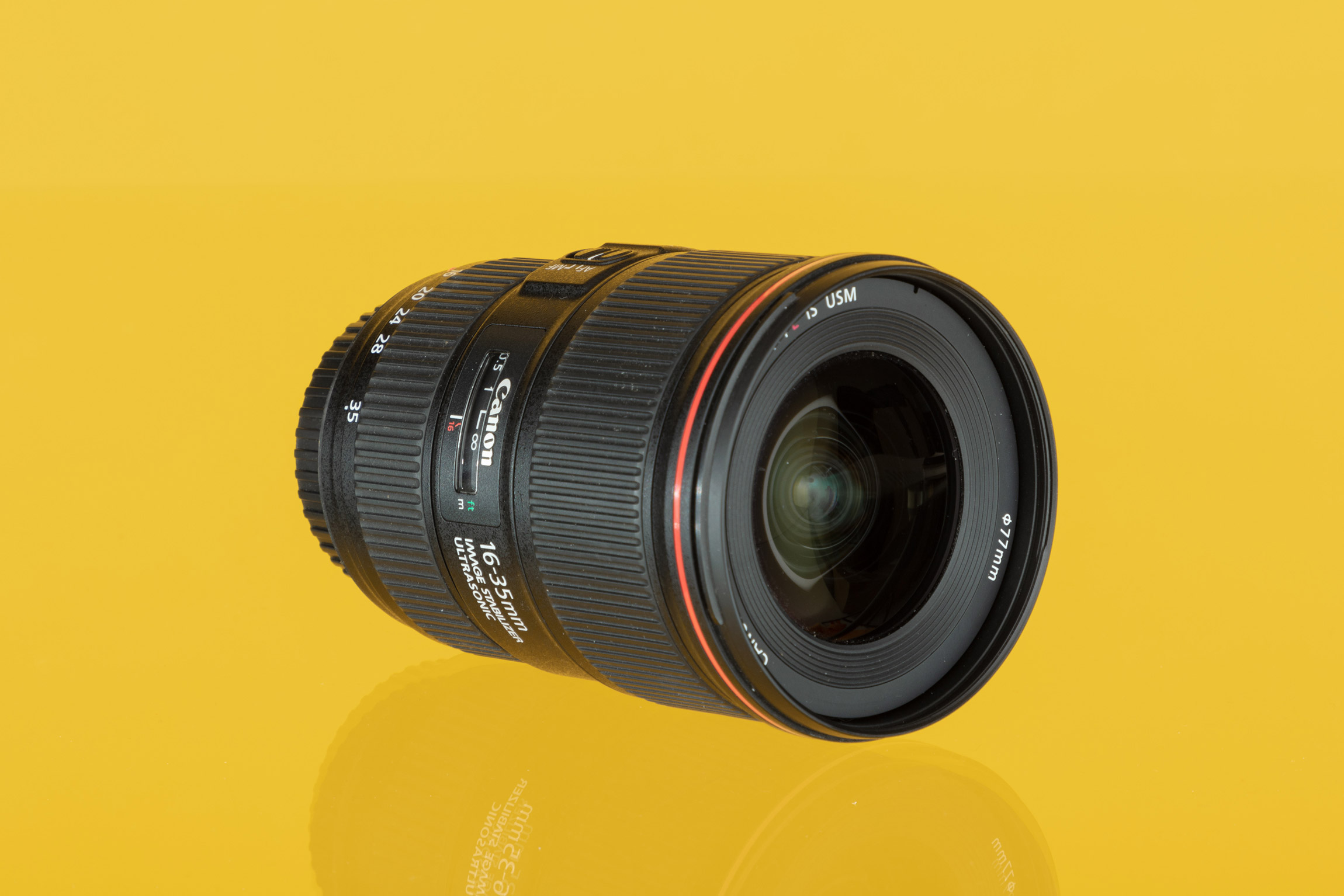 Photo d'un objectif zoom grand angle Canon EF 16-35mm f/4 L IS USM sur fond jaune.
