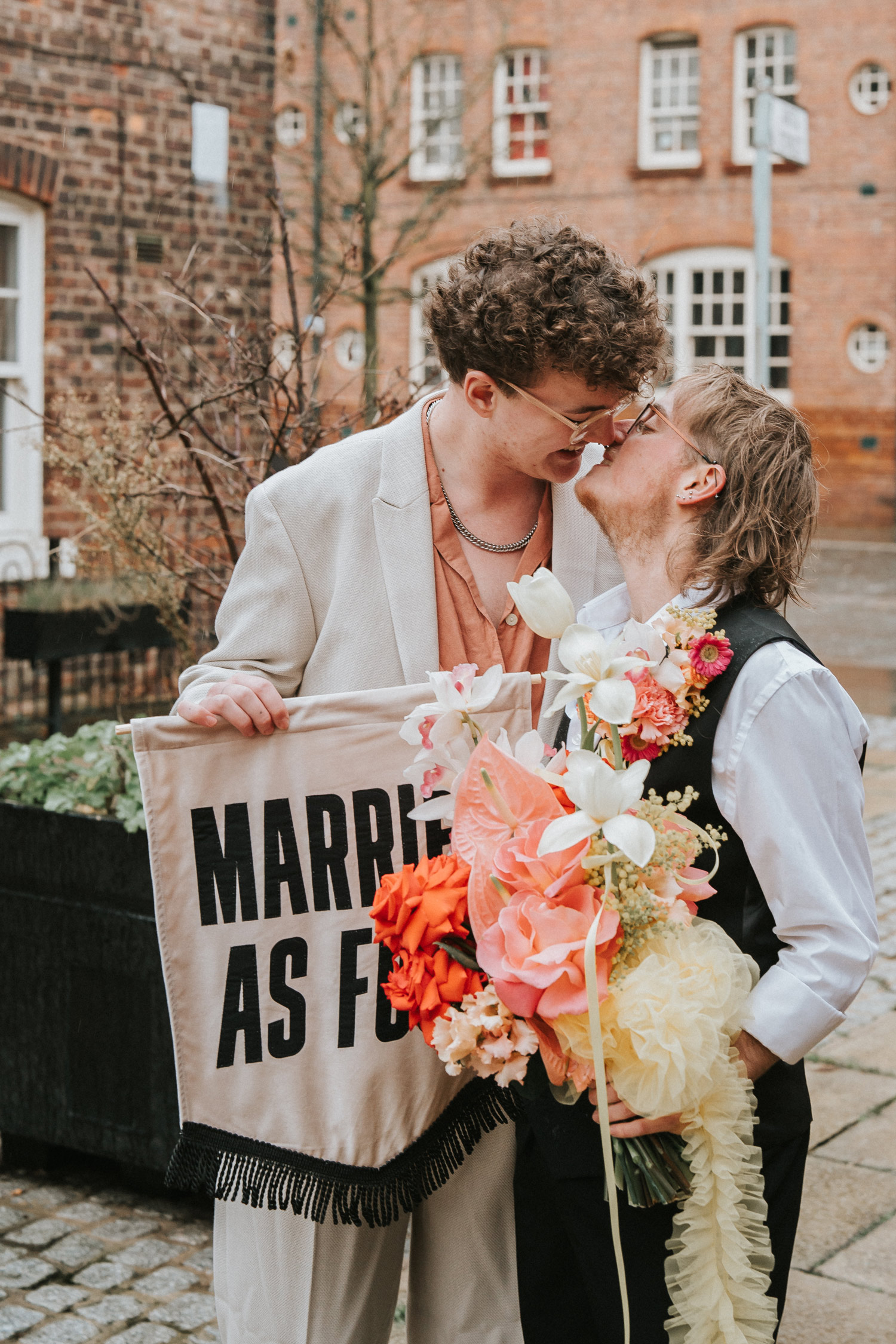 Newlyweds smiling and kissing holding a sign and a large bouquet with orange lilies and roses. Shot by Steph Large