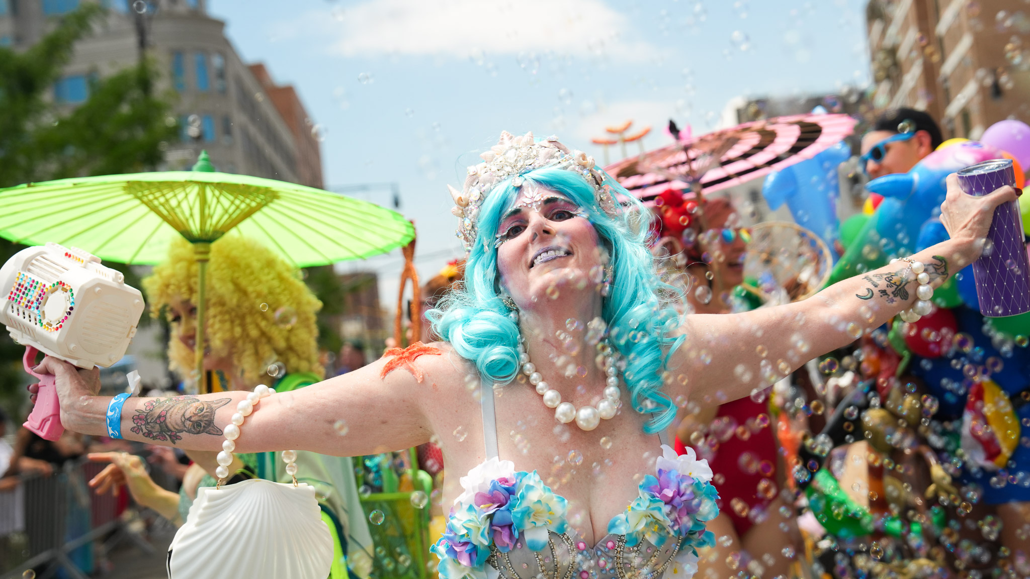A person posing for a picture at the Mermaid Parade with a bubble machine in hand and a big blue wig. By Justin Patricolo. 