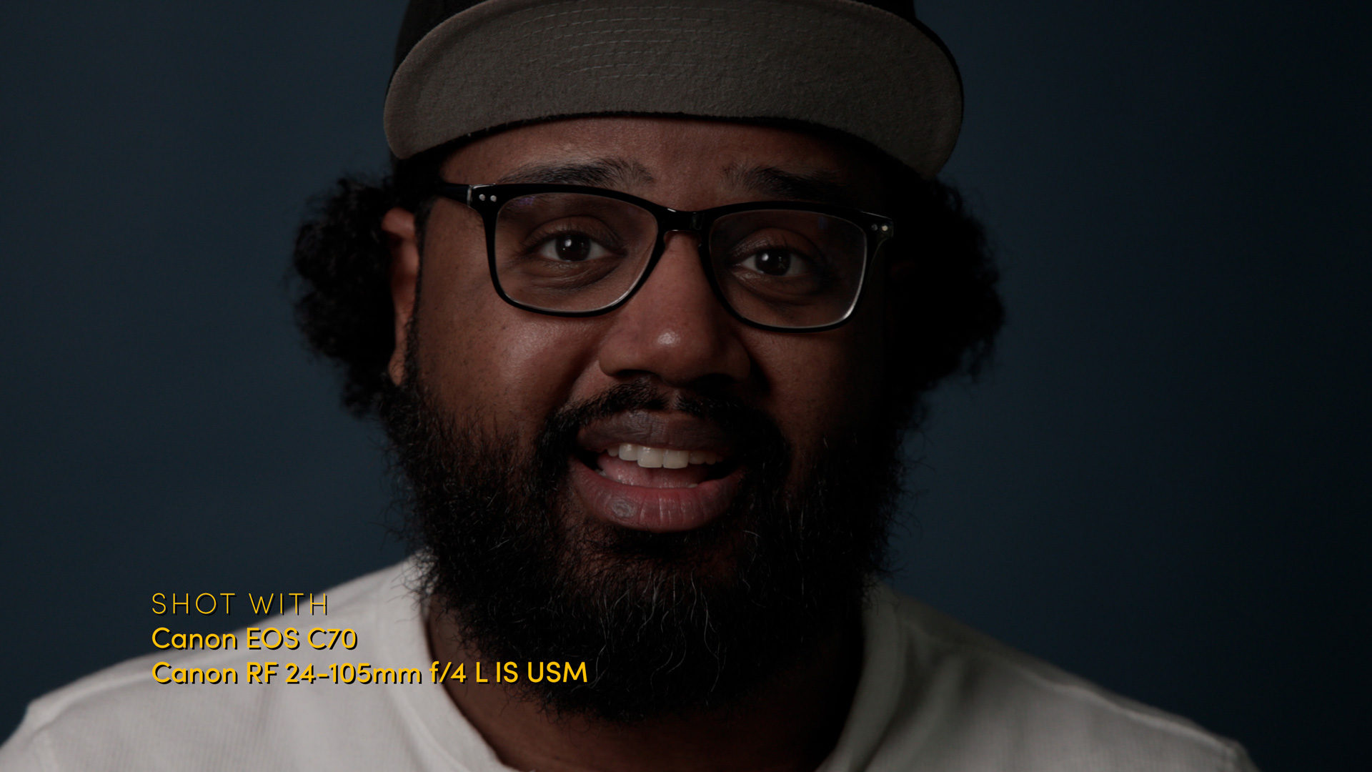 Close-up of a person with glasses and a beard sitting against a dark blue background. Taken with Canon EOS C70 and Canon RF 24-105mm f/4 L IS USM