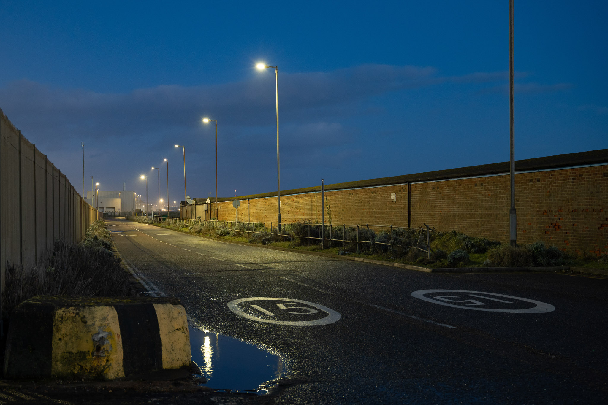 Empty industrial road at night with streetlights reflecting in puddles, photographed with the Nikon Zf by Amy Moore. 
