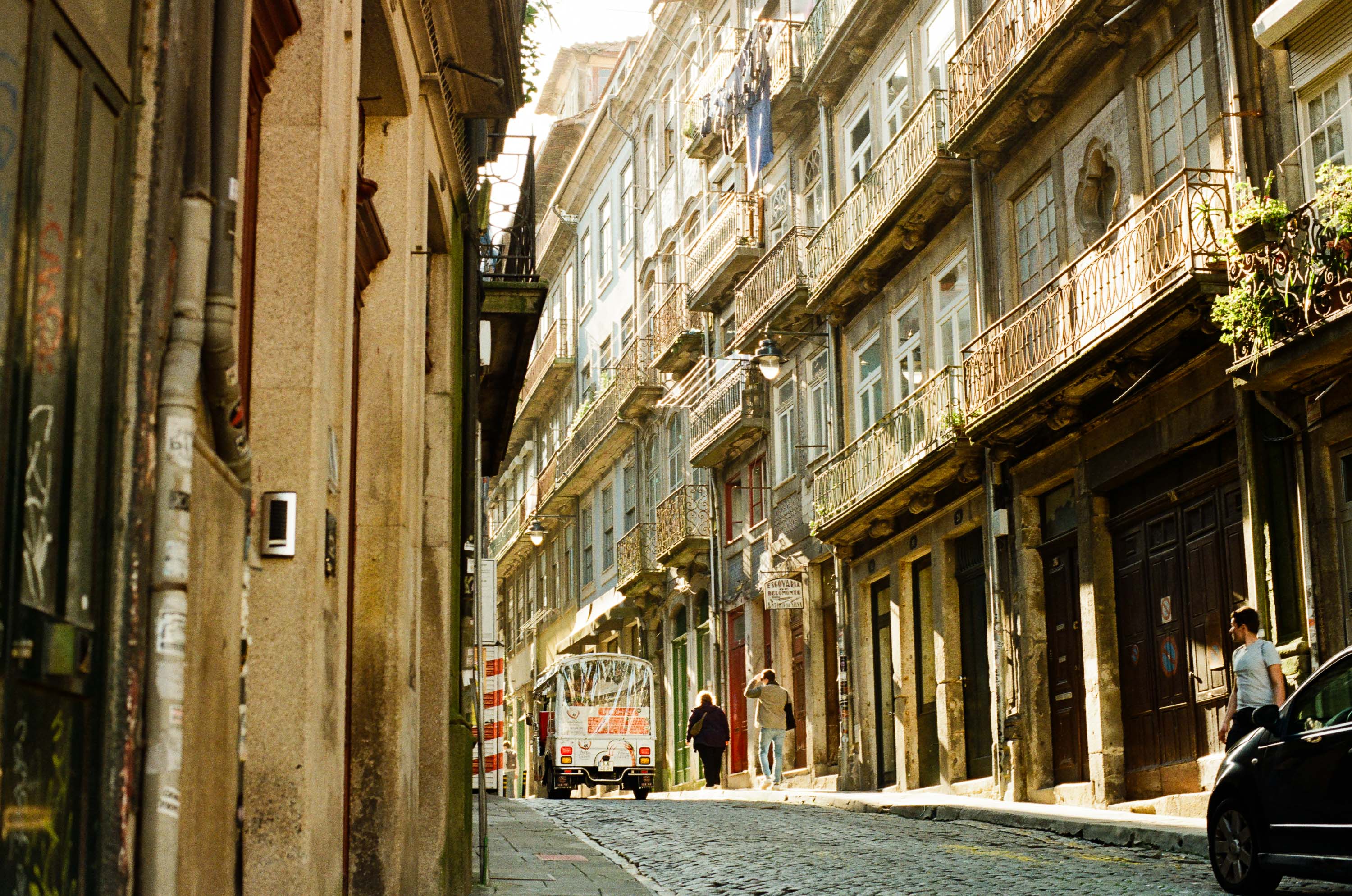 Worn architectural façade and street on Rua de Belomonte, showing intricate balcony railings, peeling paint, and varied textures under soft light.
