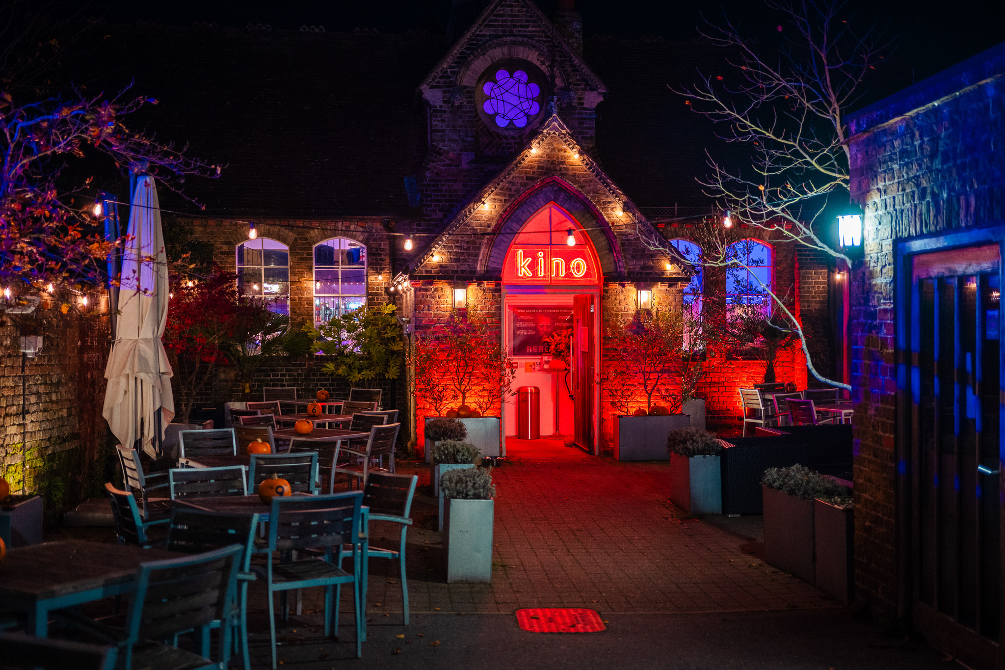 Night scene of a small cinema called Kino with the entrance illuminated by red neon lights, by Jakub Golis. 

