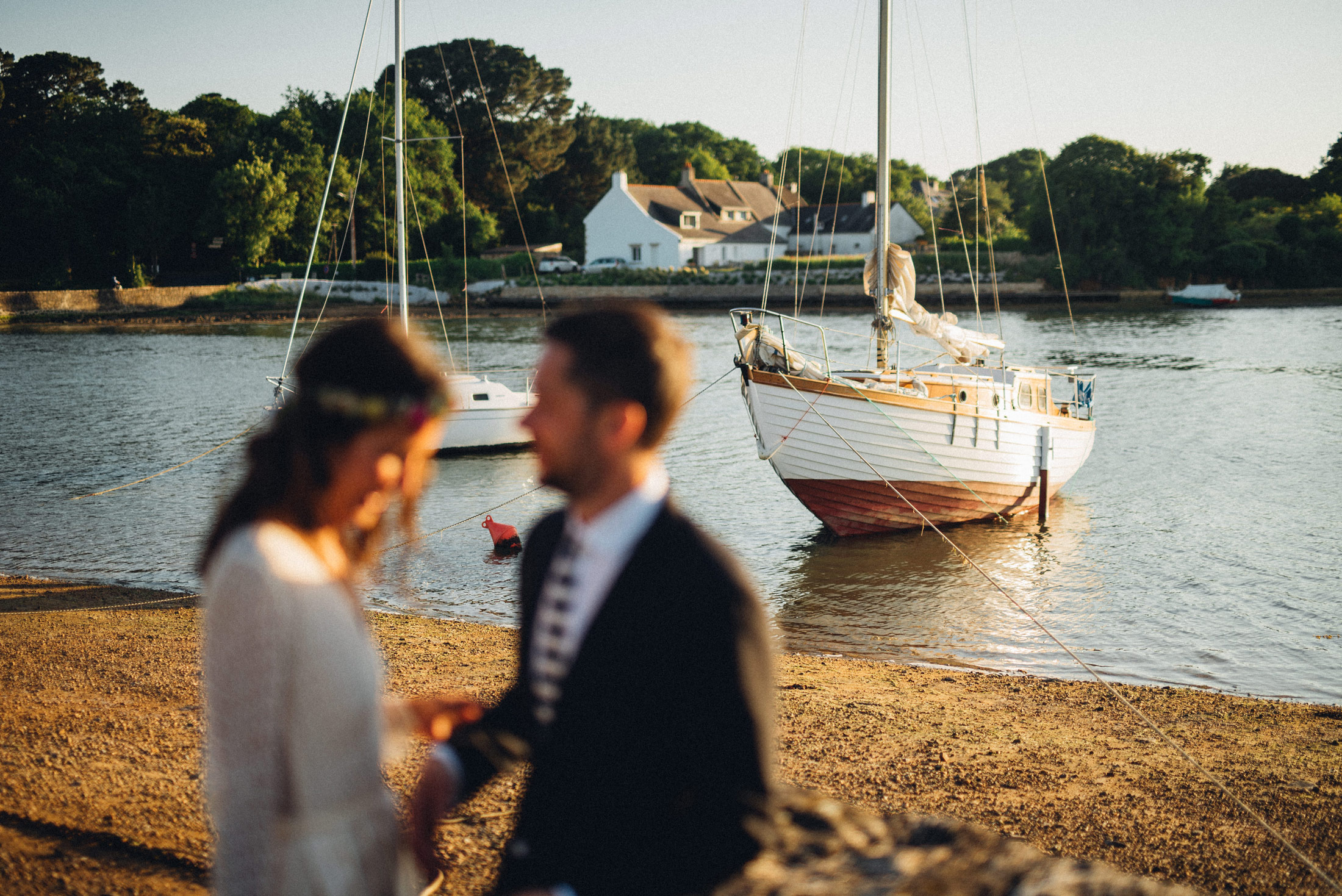 Un couple de mariés sur la plage. Les personnes sont floues mais on devine des bateaux et la mer en arrière-plan/ Photo prise par Gauthier Le Guen en Bretagne avec un Canon R6.