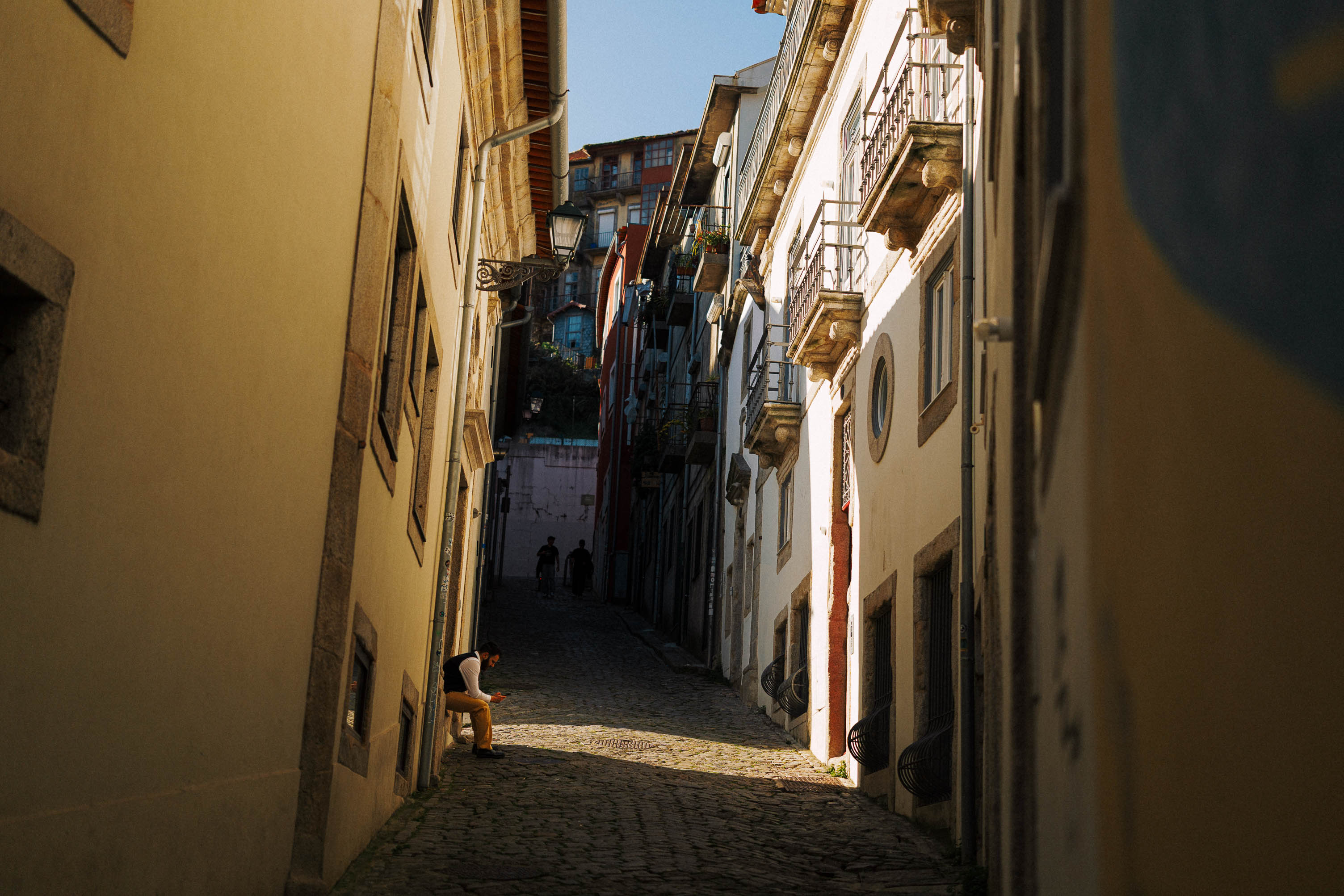 Leicht schräge Aufnahme einer Gasse in Porto mit einer Person, die auf einer Mauer sitzt. Aufgenommen von Connor Redmond mit der Sigma BF.