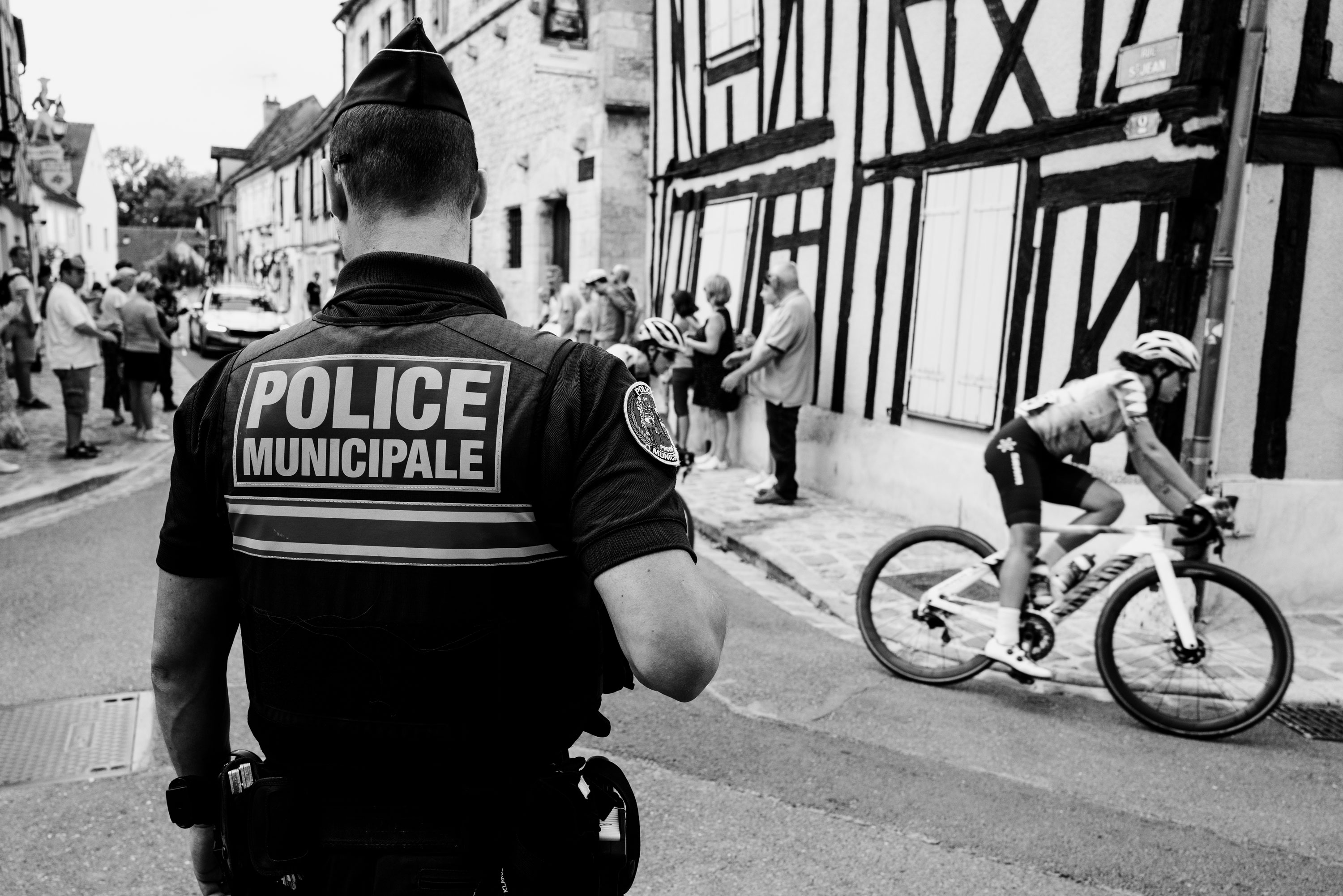 Black and white image of a cyclist from the Women’s Tour De France passing a police officer.