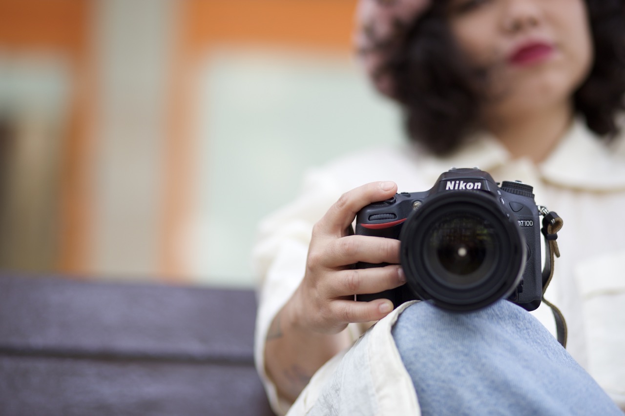 A photographer sitting on a bench, holding a Nikon camera on their knee