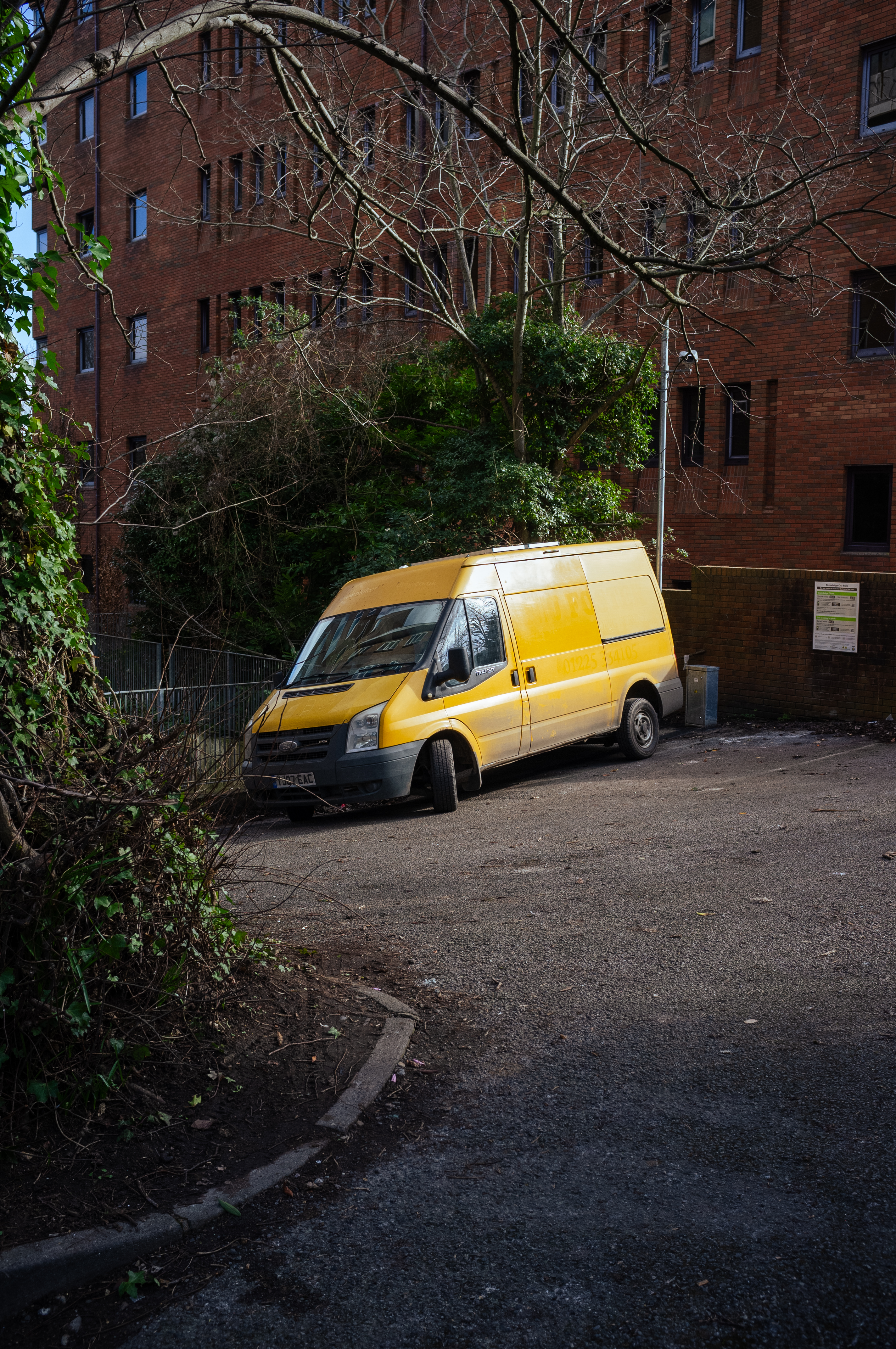 A yellow van is parked in an empty car park in front of a large corporate-looking building