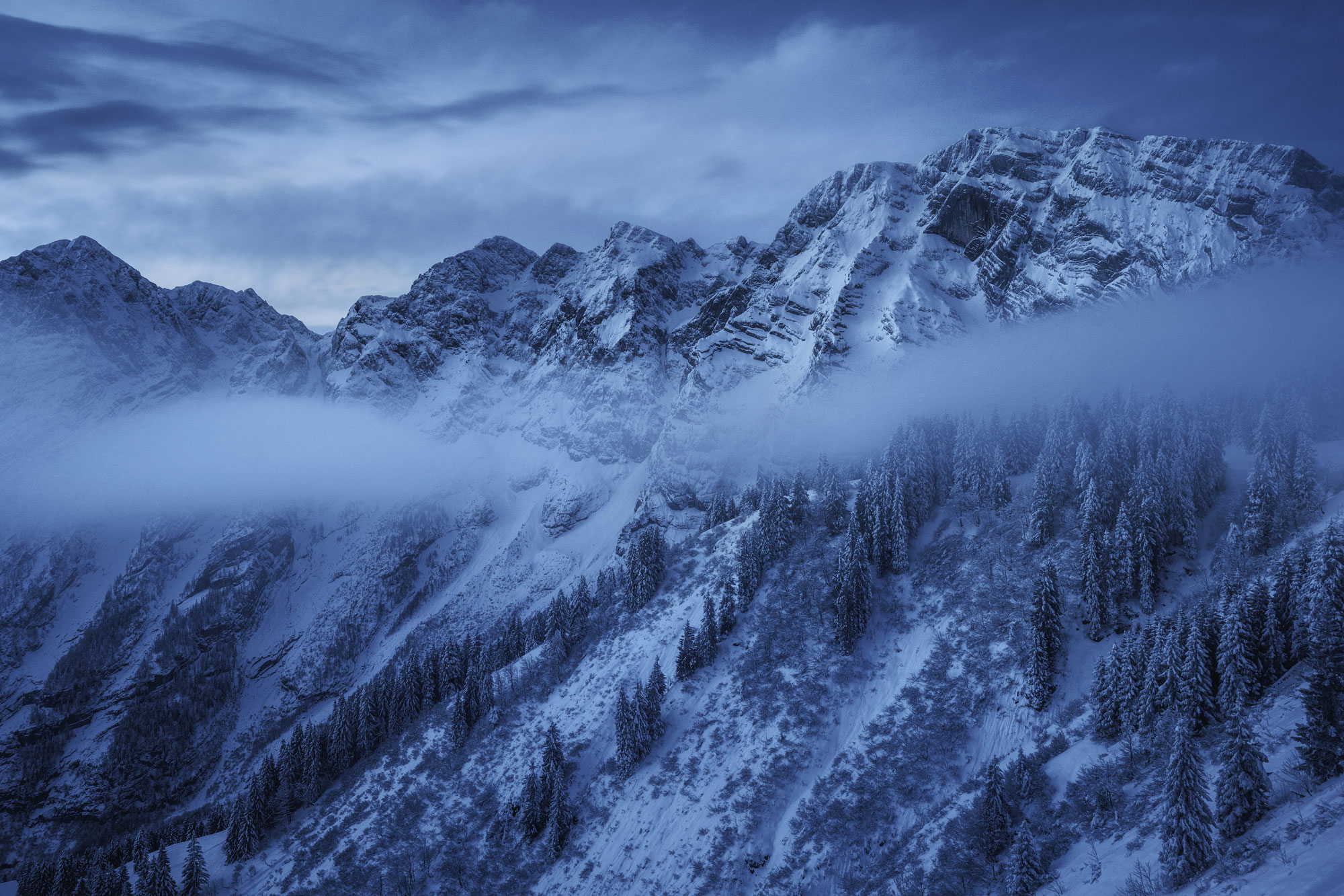Schneebedeckte, nebelverhangene Berge zur blauen Stunde, aufgenommen von Kilian Schönberger

