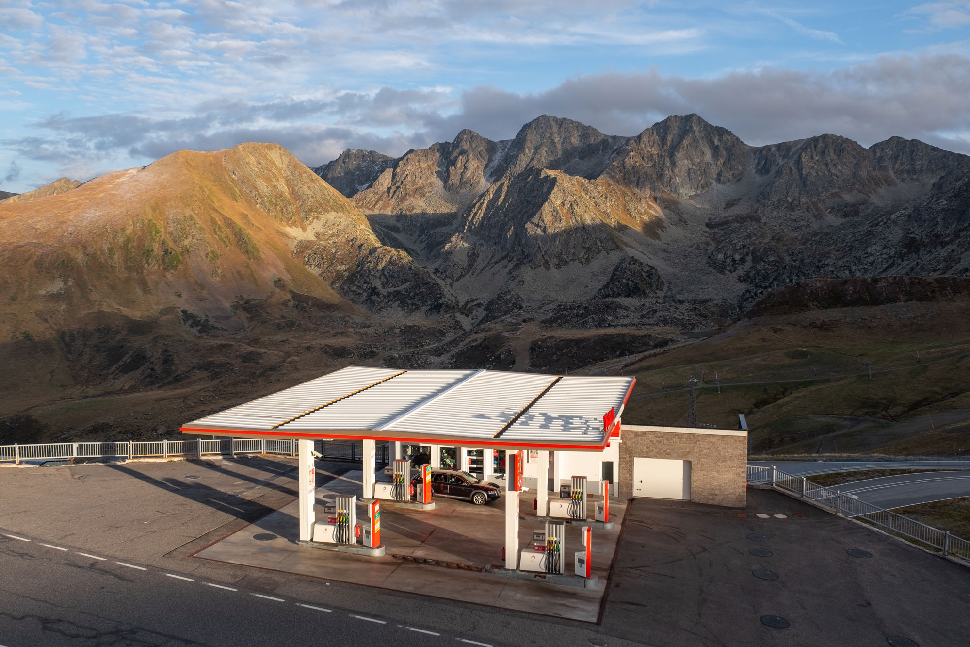 A petrol station with one car in front of a vast mountainous landscape in Spain. The light is soft, with sparse grey clouds in the background.