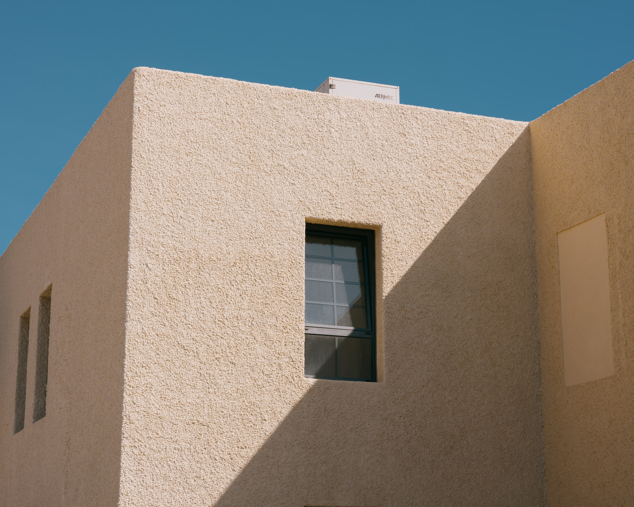 Sandfarbenes Gebäude in der Mittagssonne mit einem Schatten, der über das Gebäude geworfen wird von Connor Redmond
