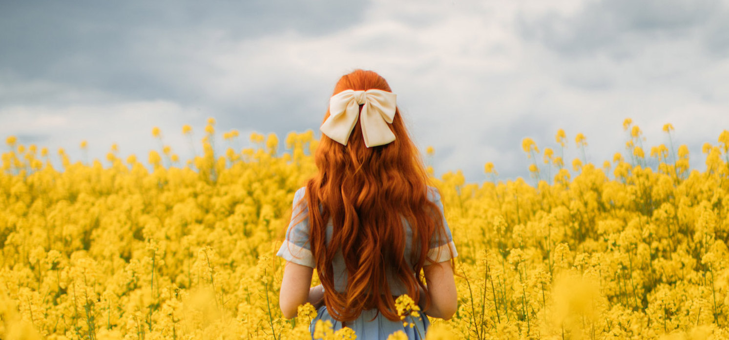 Foto di moda di Rebecca Stice con un fiocco bianco, in piedi in un campo giallo