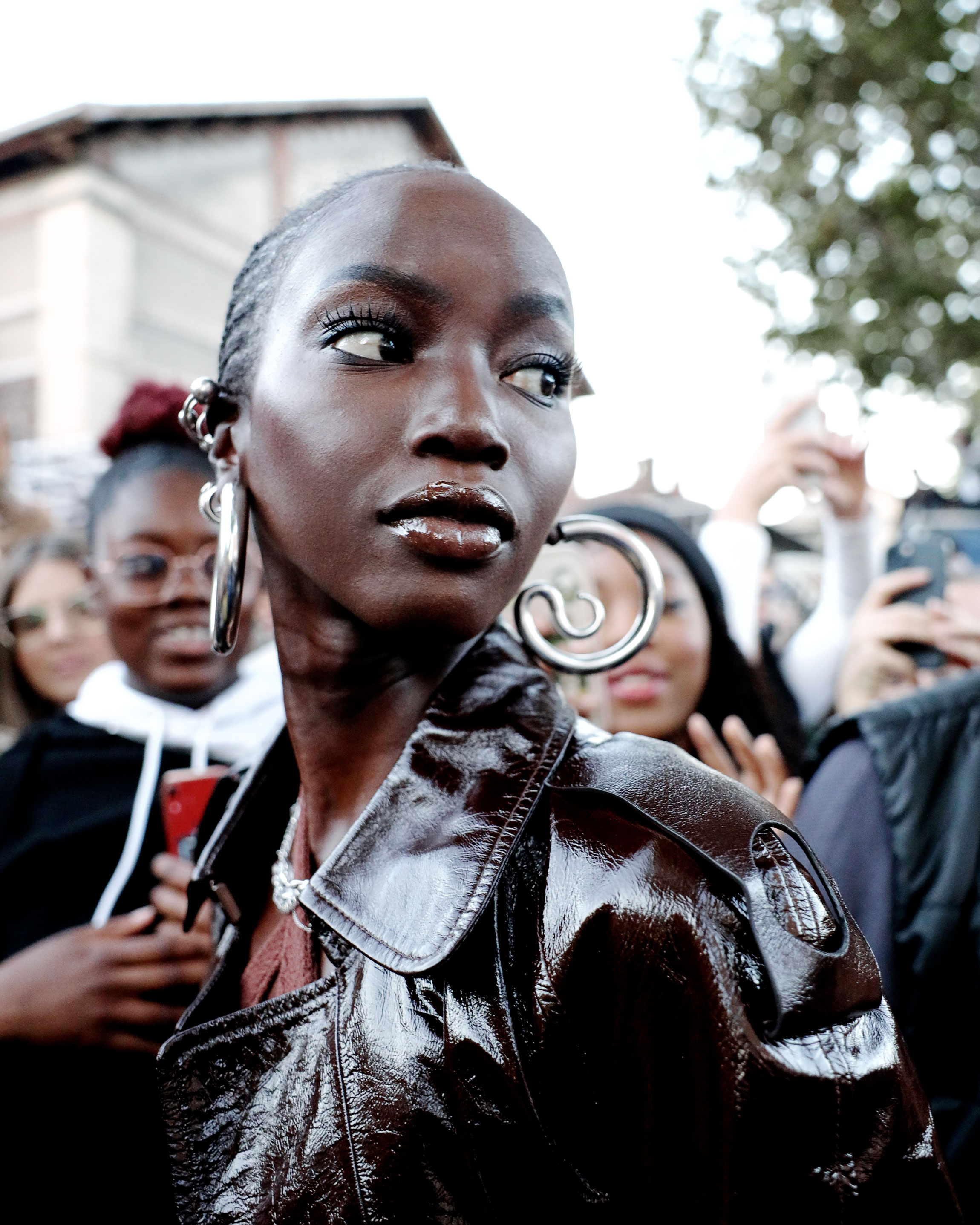 Portrait of a black woman with large silver earrings and leather jacket, looking to the left, people in the background, shot by Lisa Marie Asubonteng