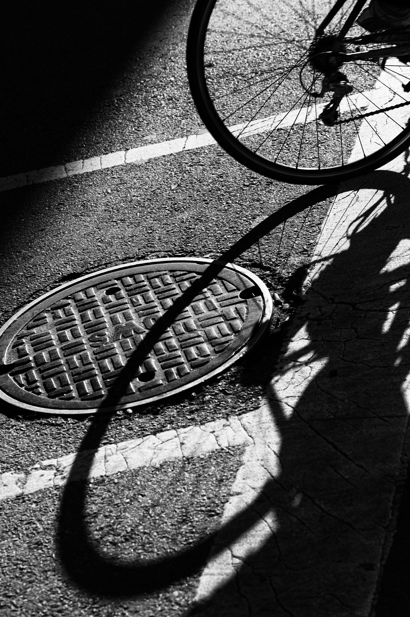 Foto en blanco y negro de una tapa de alcantarilla y una rueda de bicicleta, tomada con la Leica M Monochrom.