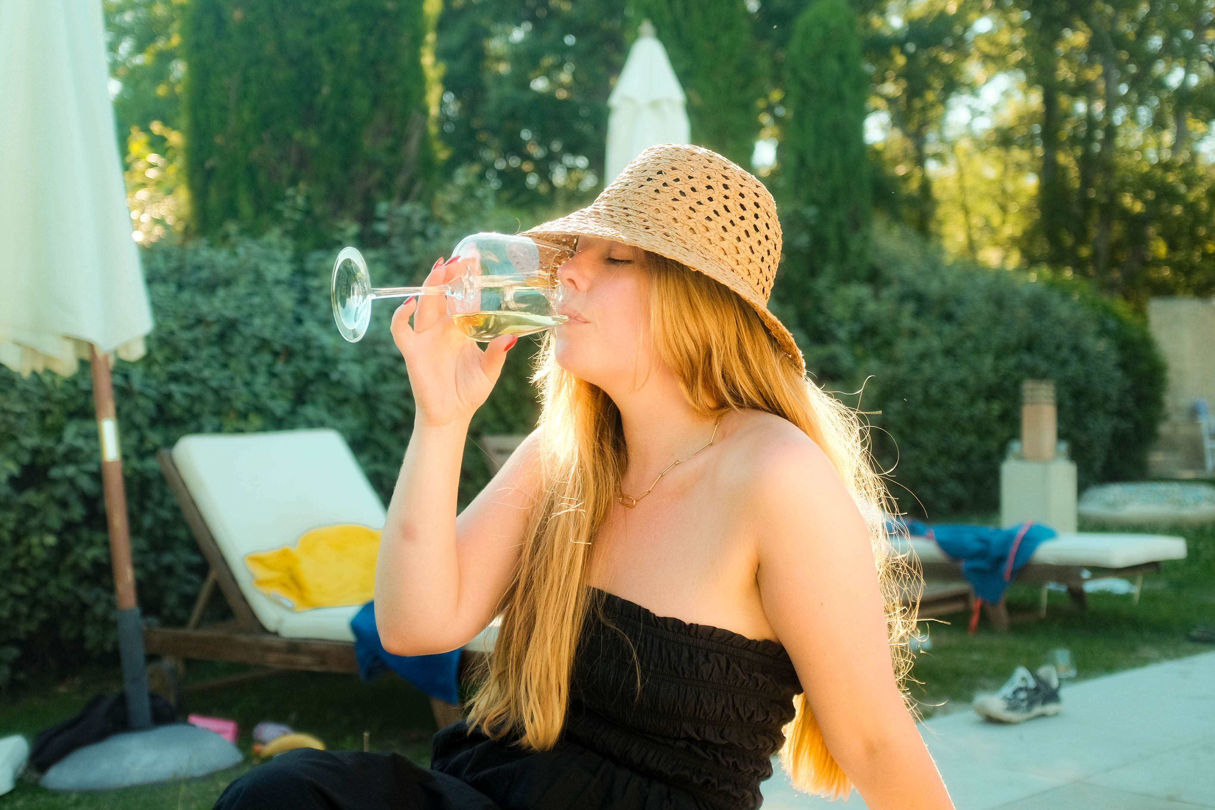 A person drinking some white wine by a pool in glorious backlit sunlight. Taken on the Fujifilm X100T by Connor Redmond.