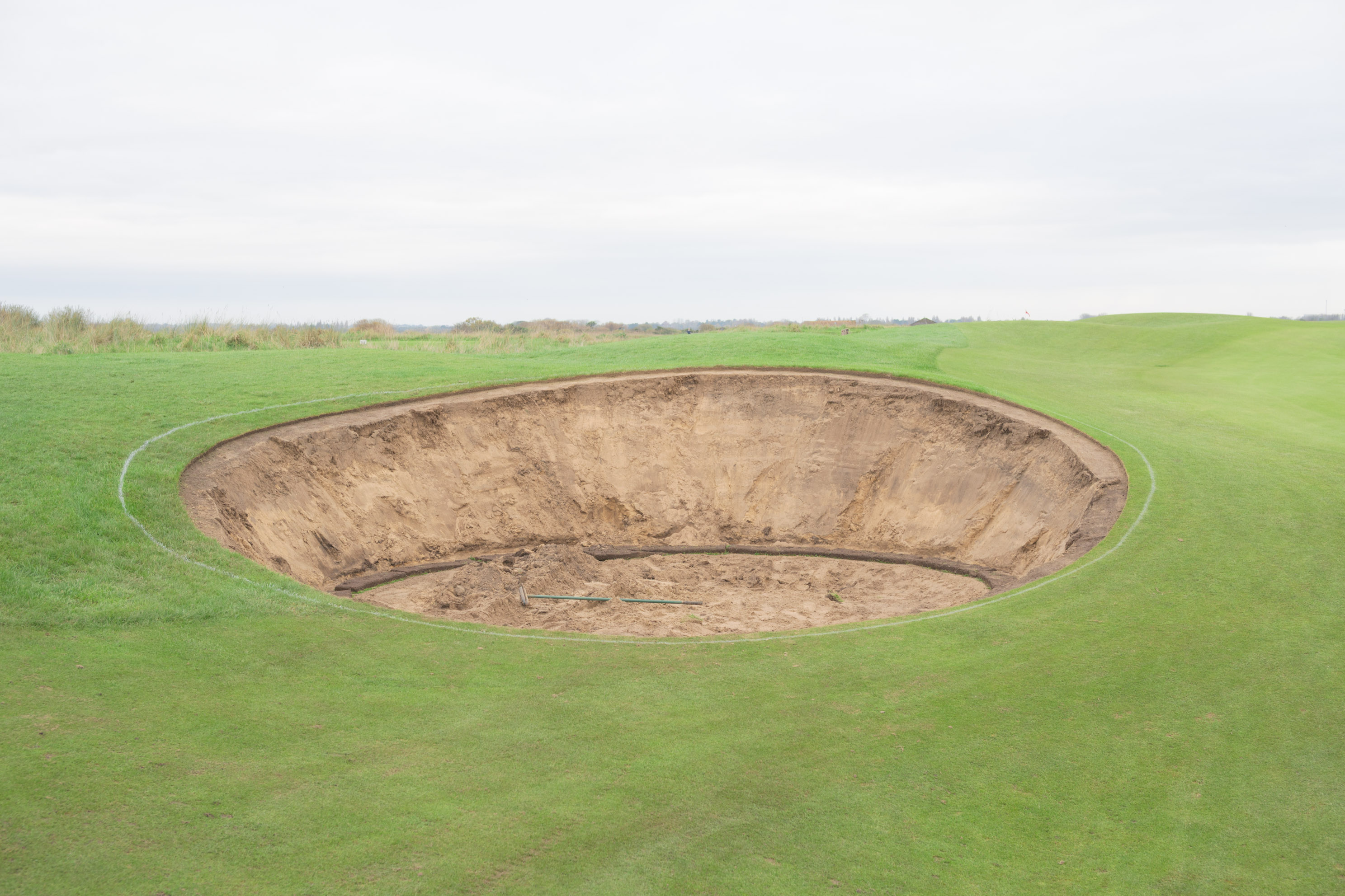 Large sand bunker on a golf course under overcast skies, by Connor Redmond. 