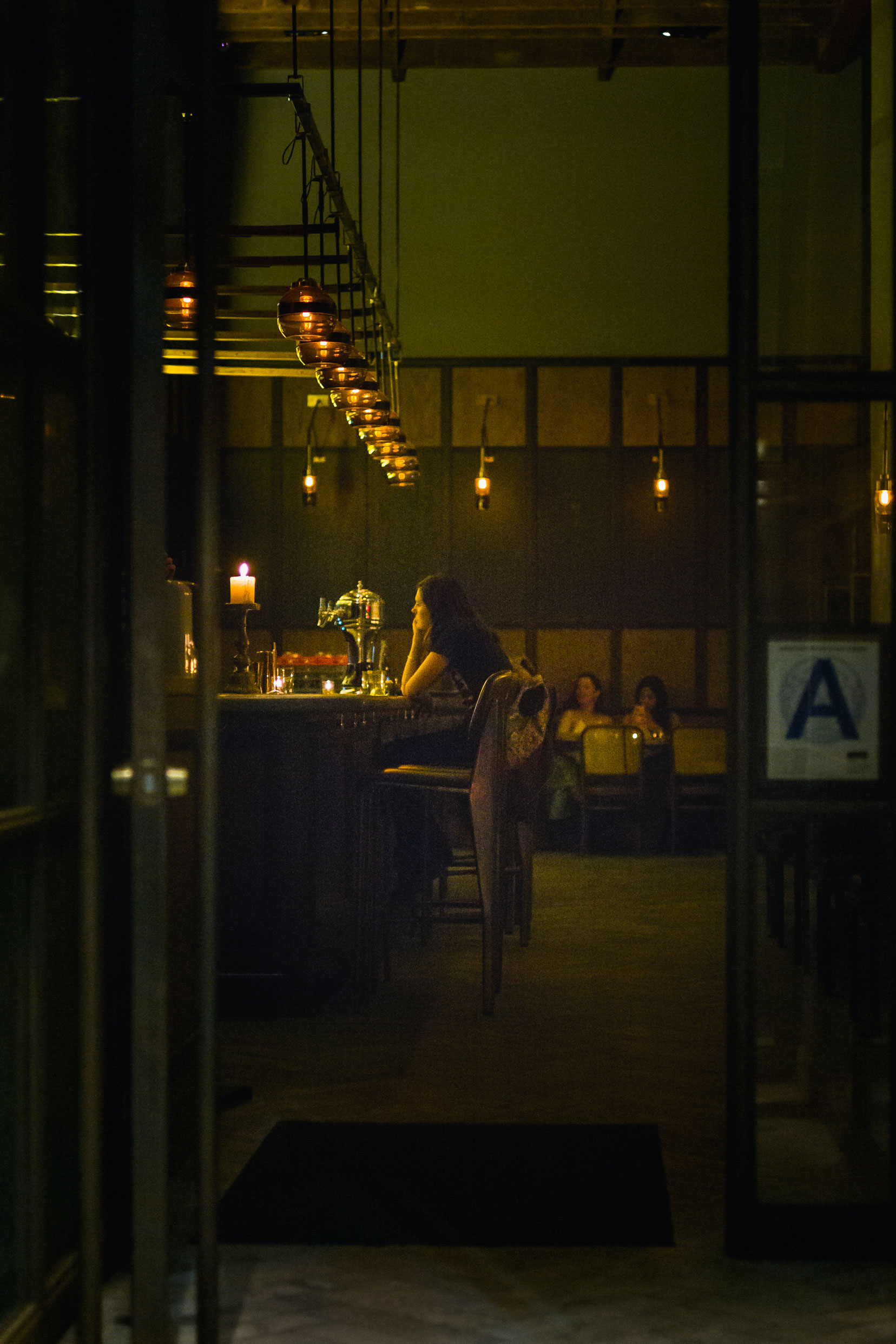 Person inside of a New York City restaurant sitting at a bar at night with warm light, photo by Manuel Pena on a Leica M10.