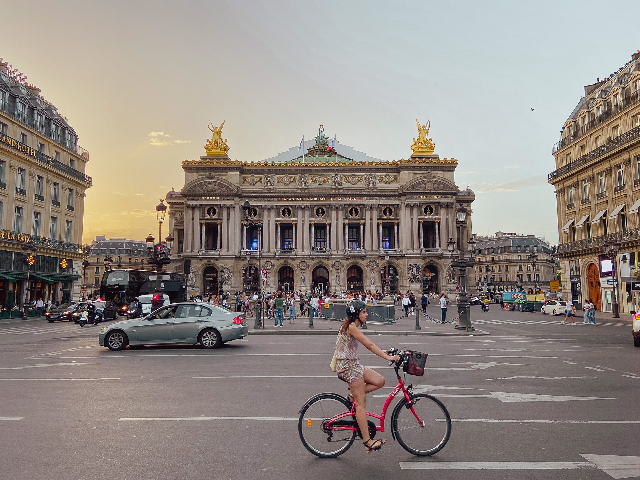 Palais Garnier opera house in Paris at sunset with a cyclist passing in the foreground, capturing busy city life and historic architecture.