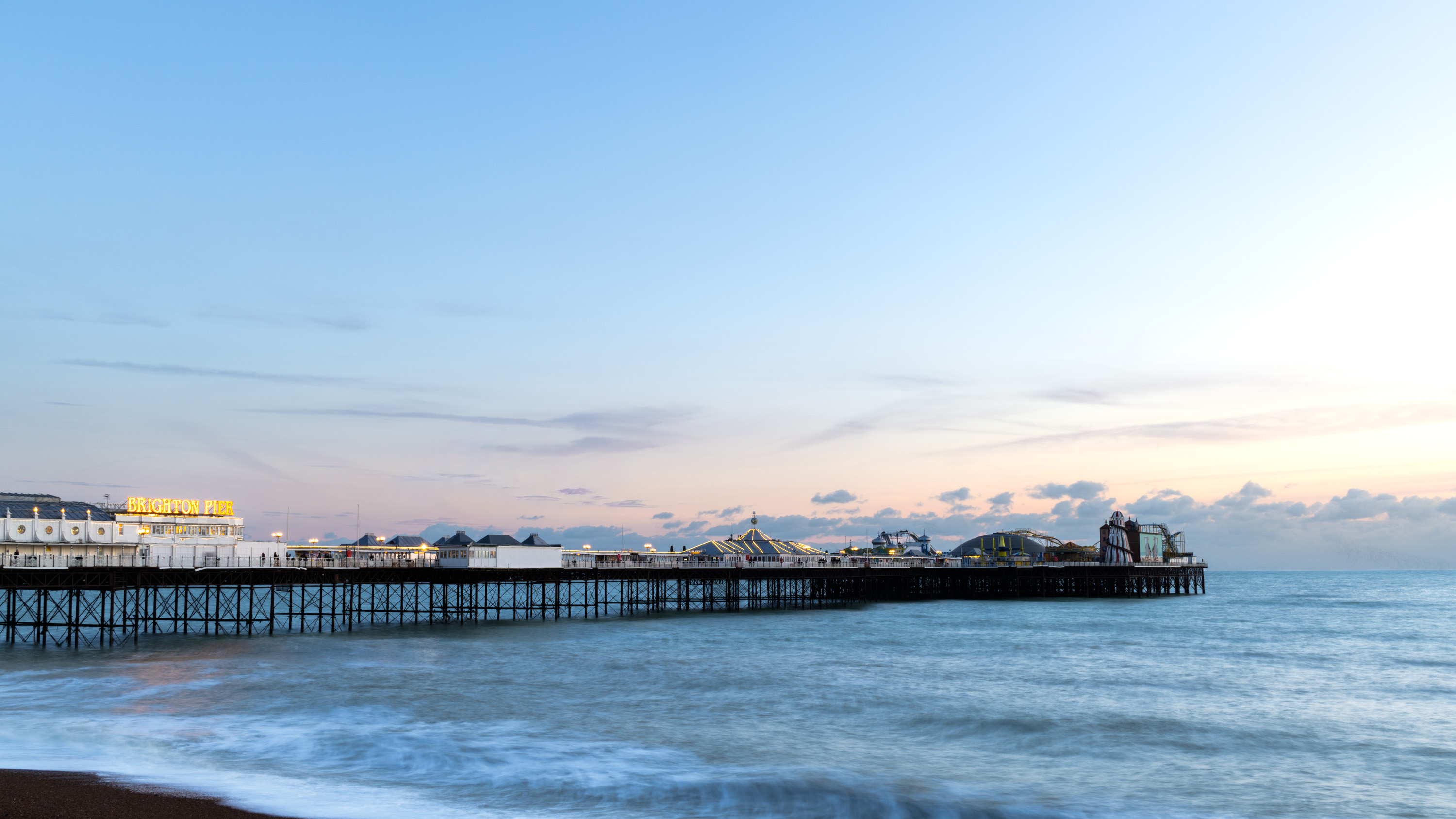 Langzeitbelichtung des Brighton Pier in der Abenddämmerung, mit ruhigem Pastellhimmel, Pierbeleuchtung und dem sanft verschwommenen Meer. Aufgenommen von Connor Redmond mit einer Sony RX1R III vom Strand aus.