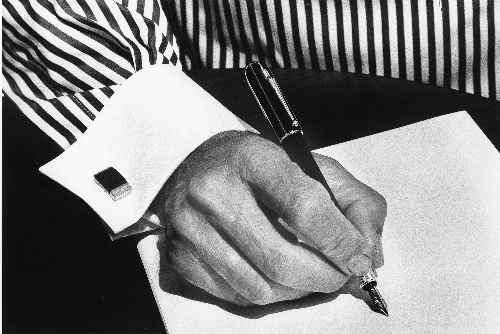 Ralph Gibson, imagen en blanco y negro de un hombre escribiendo con una pluma estilográfica, con camisa de rayas y gemelos. Tomada con Leica.