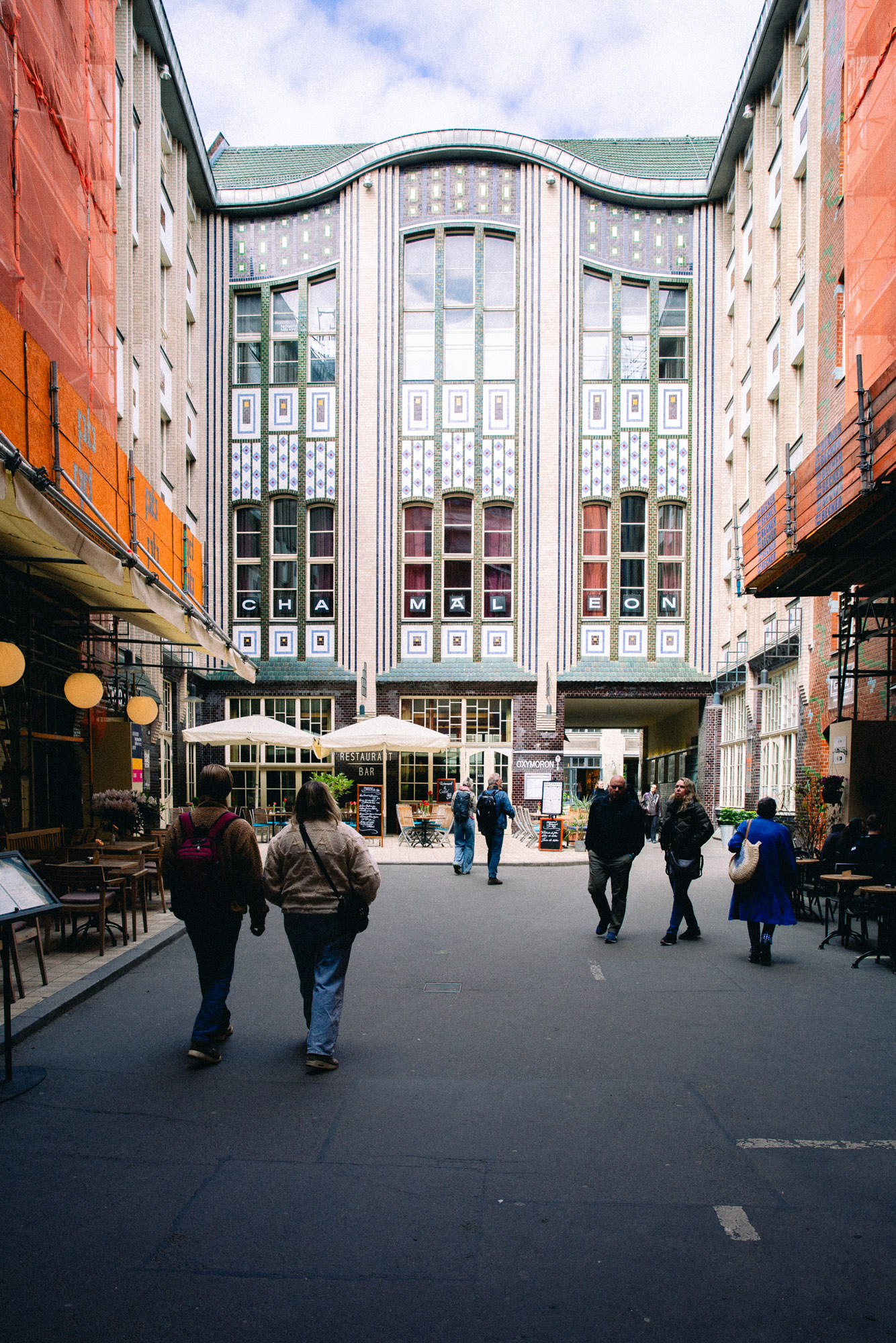 Photograph of people walking through Berlin’s Hackesche Höfe courtyard, framed by cafes, scaffolding and an ornate tiled facade. Shot by Austin Fassino on a Canon EOS 5D Mark III.