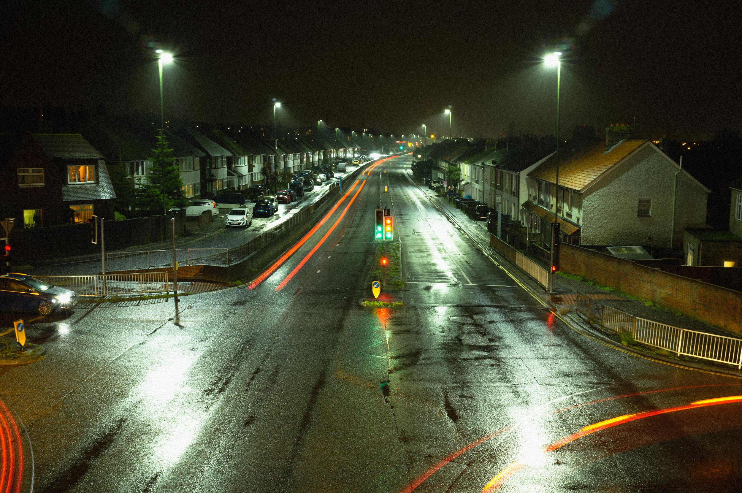 A crossroads on a dark and wet winter evening. There is minimal traffic, and blurred headlights follow the paths of cars, shot by Jakub Golis with Fujifilm X100