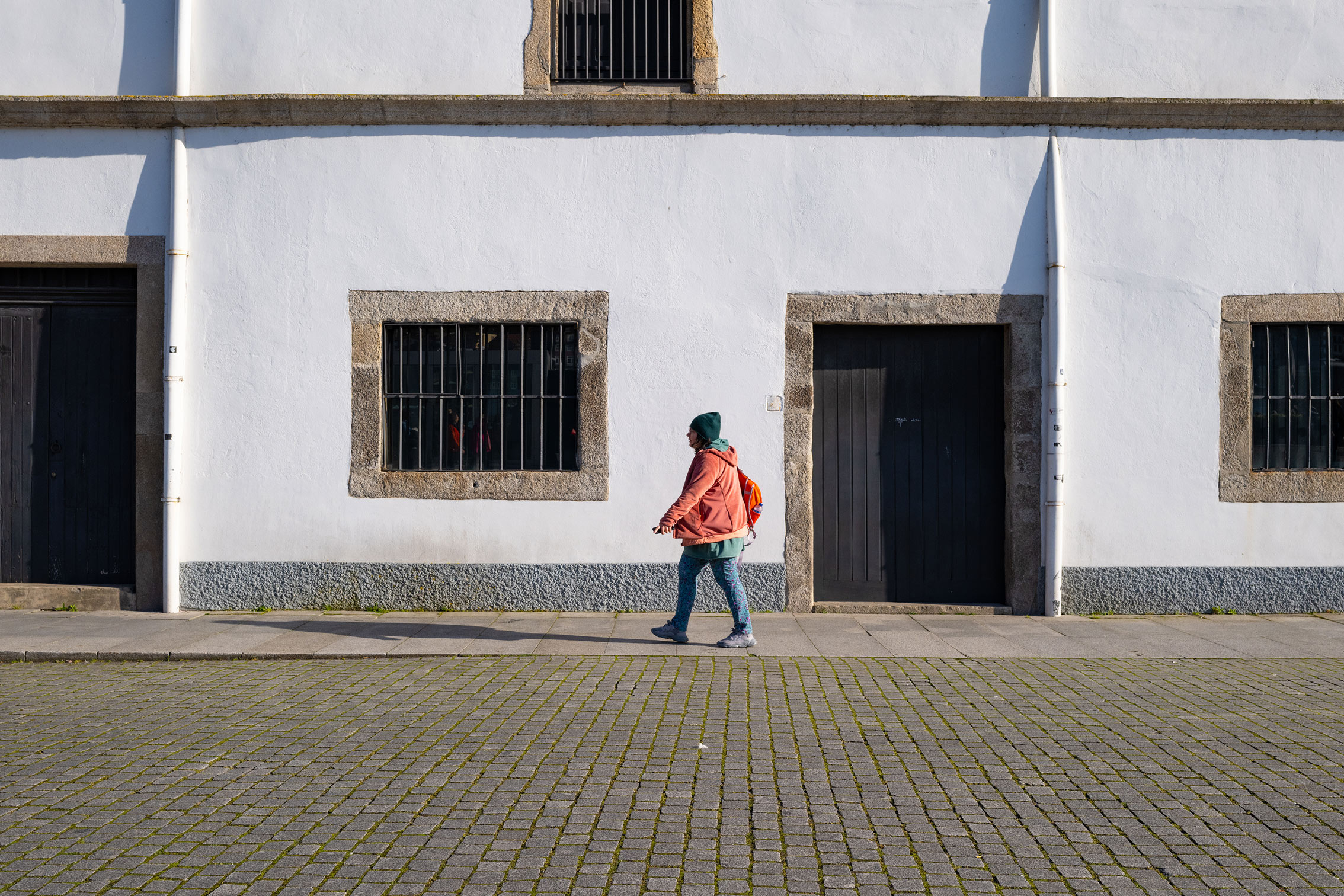 A person in orange walking past a white-fronted building in Porto, Portugal. Shot on the Fujifilm GFX100RF by Amy Moore.